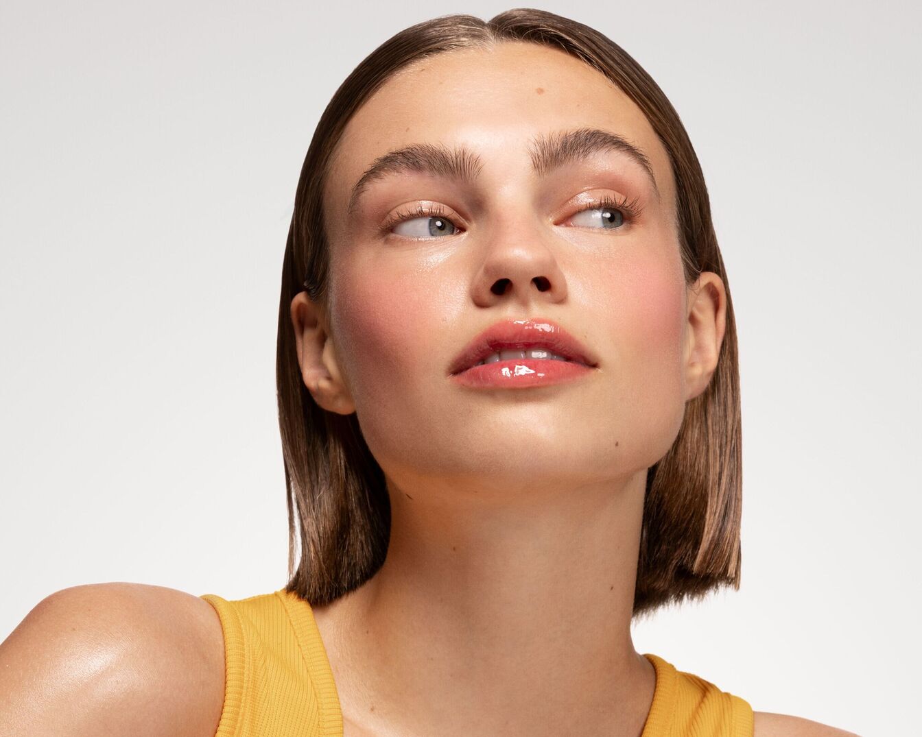 Portrait d'une jeune femme avec un maquillage frais : joues rosées et lèvres brillantes, le tout rehaussé par un teint éclatant et une coupe de cheveux courte et élégante.