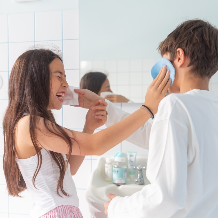 Deux enfants utilisant des lingettes sur le visage dans une salle de bain, moment de soin partagé.