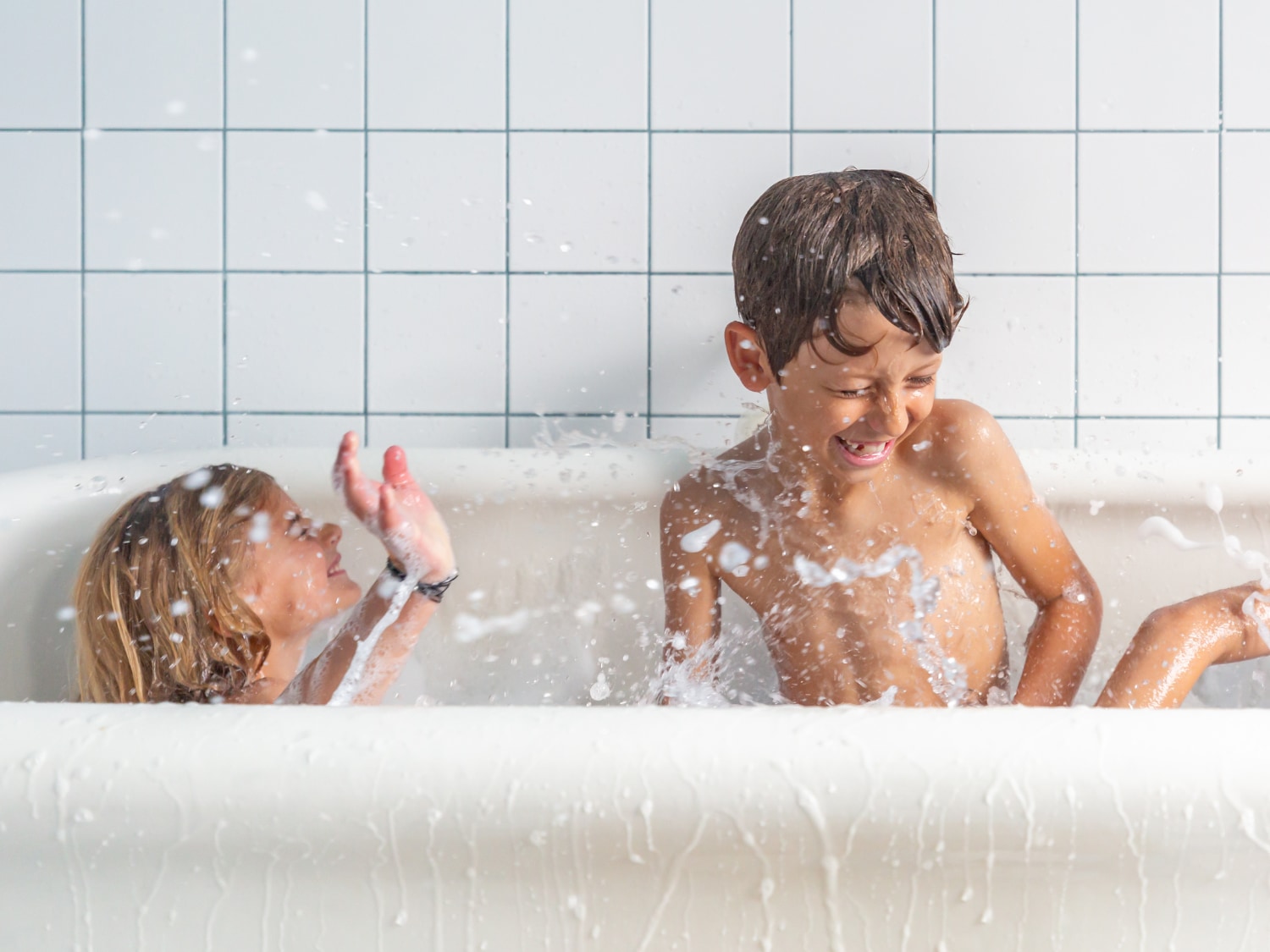 Enfants jouant dans le bain avec une mousse lavante, moment ludique de la routine corps OUATE.