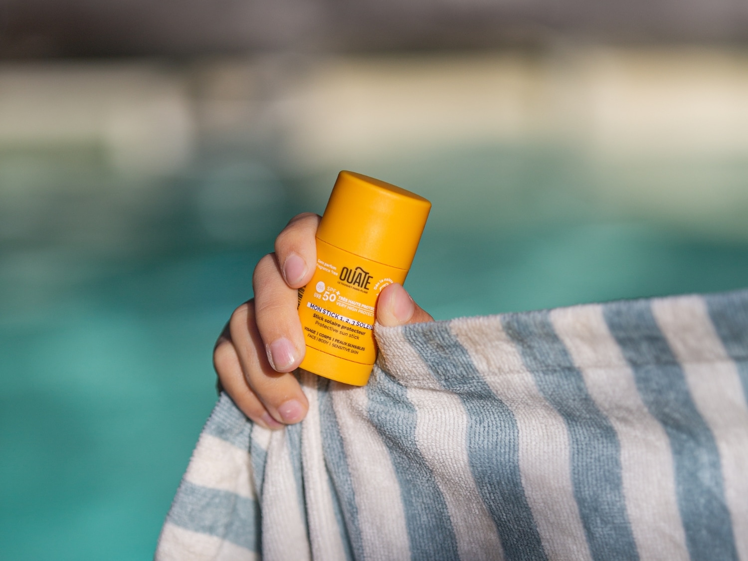 Main tenant un stick solaire dans un environnement extérieur, moment d’application d’un soin solaire.