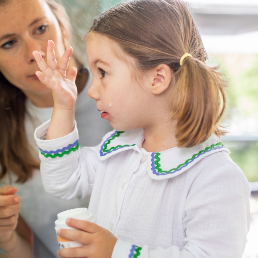 Enfant appliquant une crème avec l’aide d’un adulte dans une salle de bain, apprentissage d’un geste de soin.