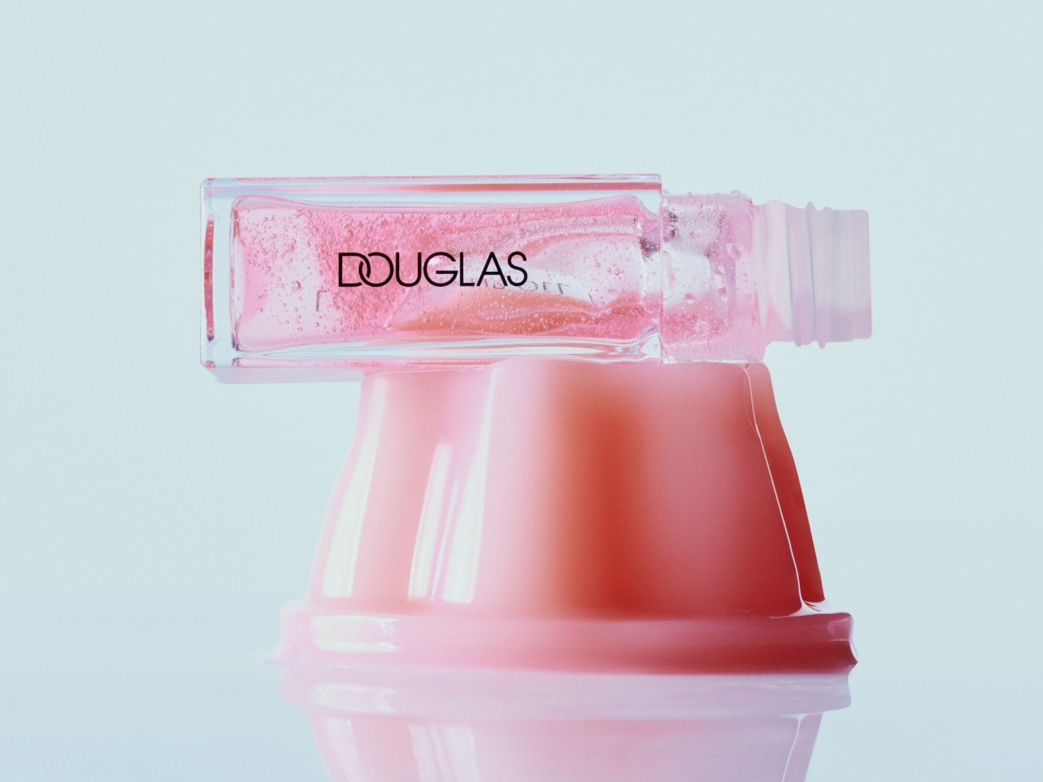 Découvrez le brillant à lèvres Douglas, un éclat rose délicat dans un flacon transparent, reposant sur une base rose douce pour une touche de glamour subtile.