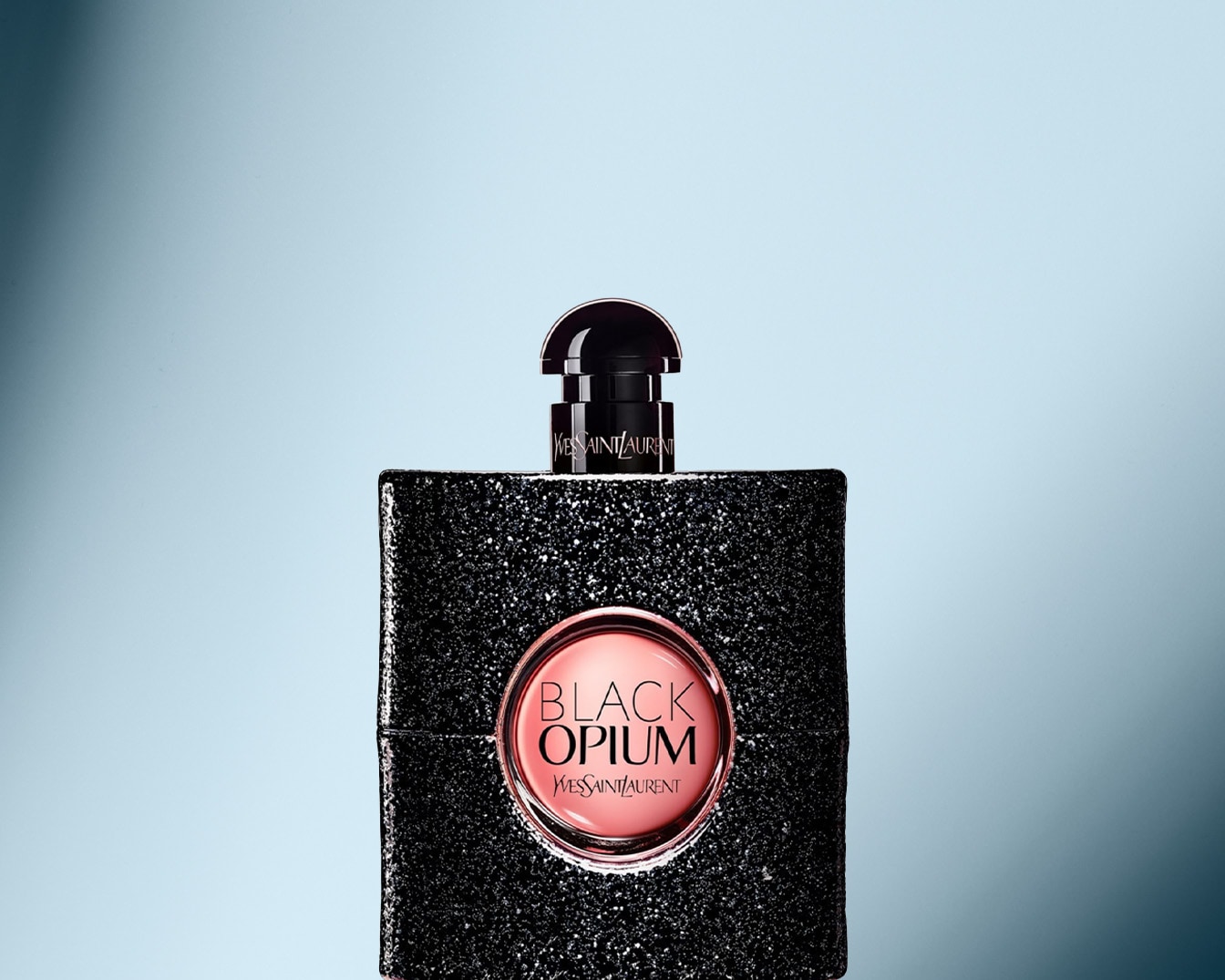 Nahaufnahme des Black Opium Parfüms von Yves Saint Laurent, dessen Flakon mit schwarzen Glitzerpartikeln bedeckt ist und ein rosa Etikett mit dem Namen des Parfüms trägt.