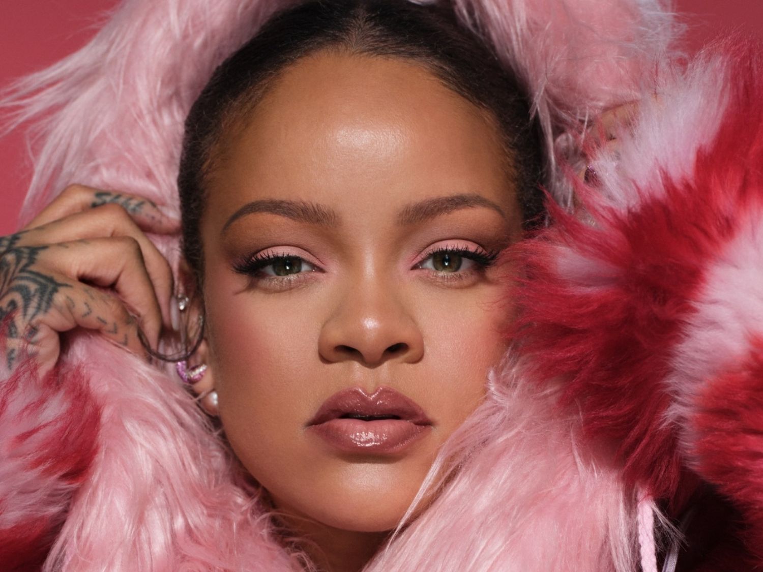 Close-up van Rihanna met een zachte roze en rode bontjas, bijpassende roze oogschaduw en glanzende lippen, die een glamoureuze en modieuze uitstraling creëert.