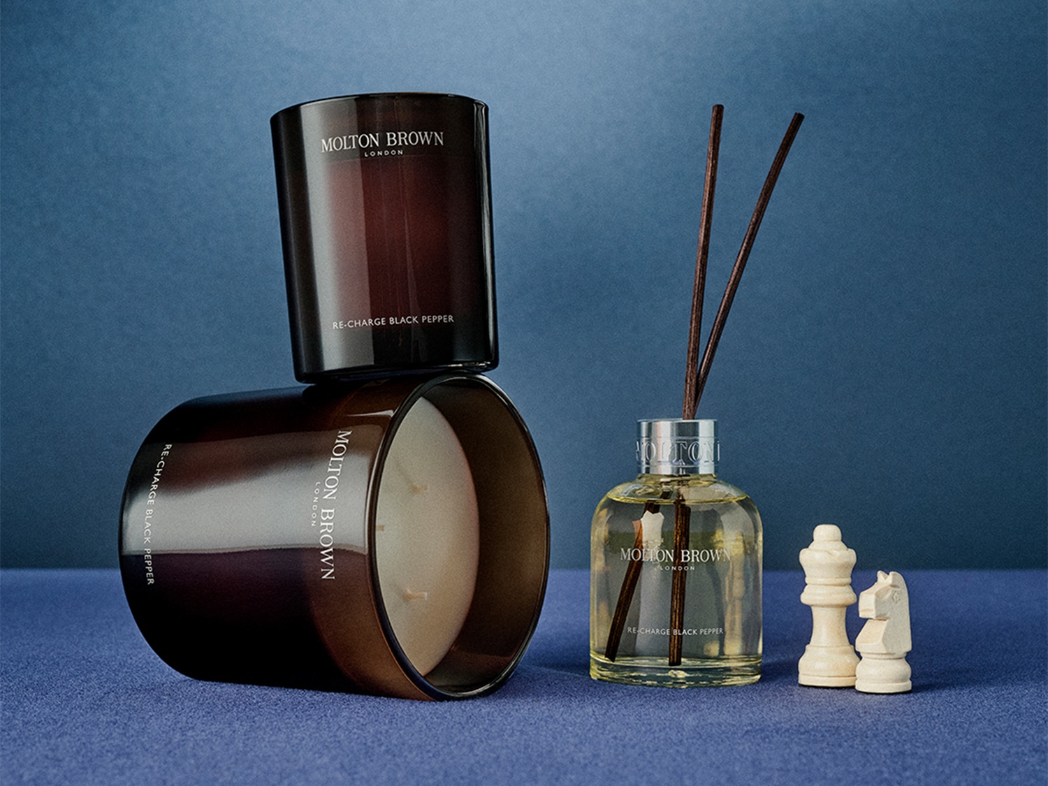 Zwei Molton Brown London Kerzen mit dem Duft Re-Charge Black Pepper und ein Duftzerstäuber mit Schachfiguren.