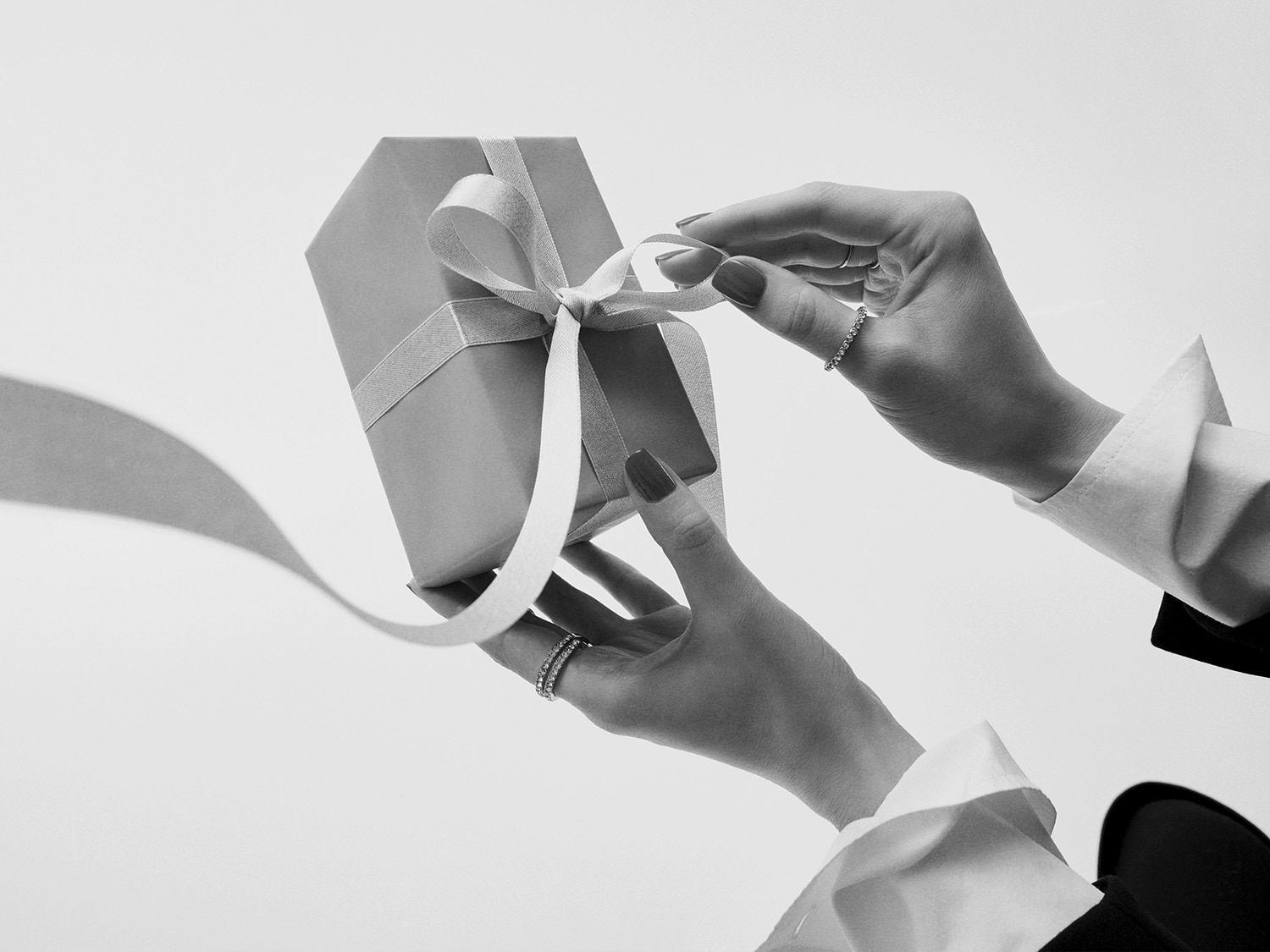 Gros plan sur les mains d'une personne déliant le ruban d'un élégant coffret cadeau gris, prêt à révéler une surprise spéciale.