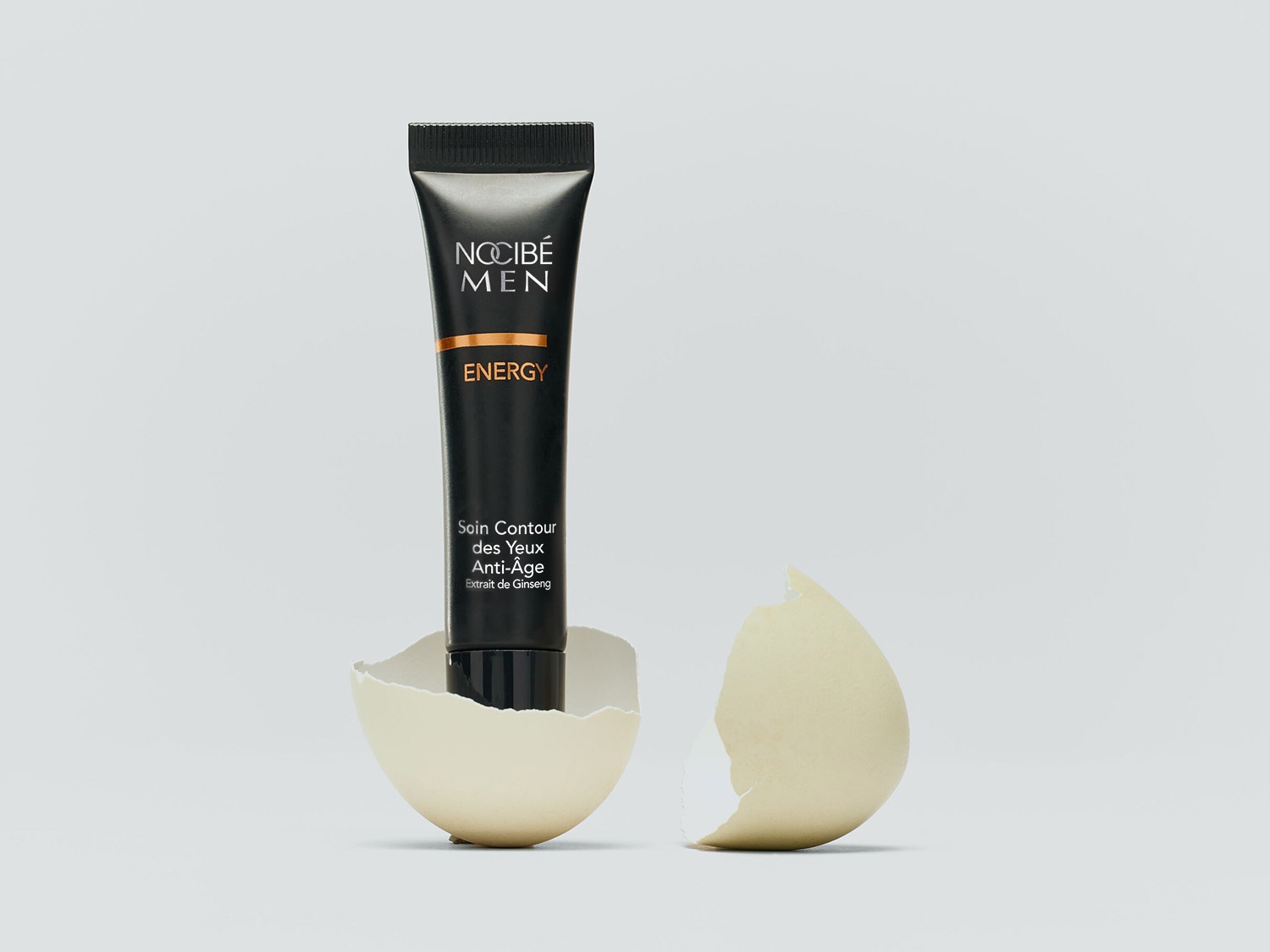 Tube noir de soin contour des yeux anti-âge Nocibé Men Energy, présenté dans une coquille d'œuf cassée, évoquant un renouveau pour le soin de la peau masculine.