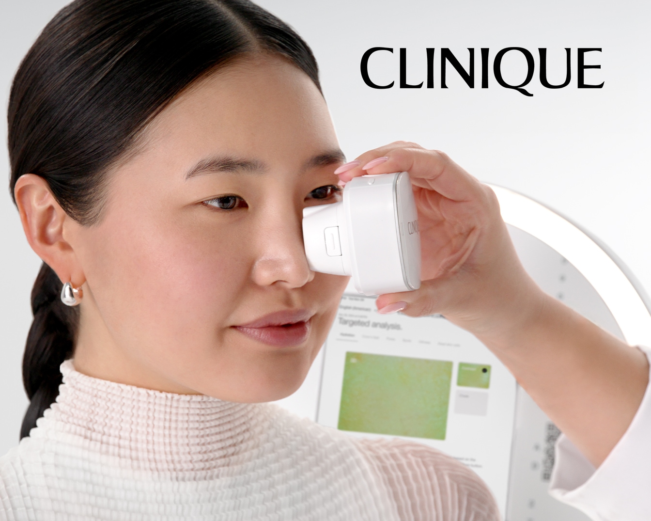 Asiatka si nechává analyzovat pleť přístrojem Clinique, který jí přikládá k oku, aby zjistila stav pleti.