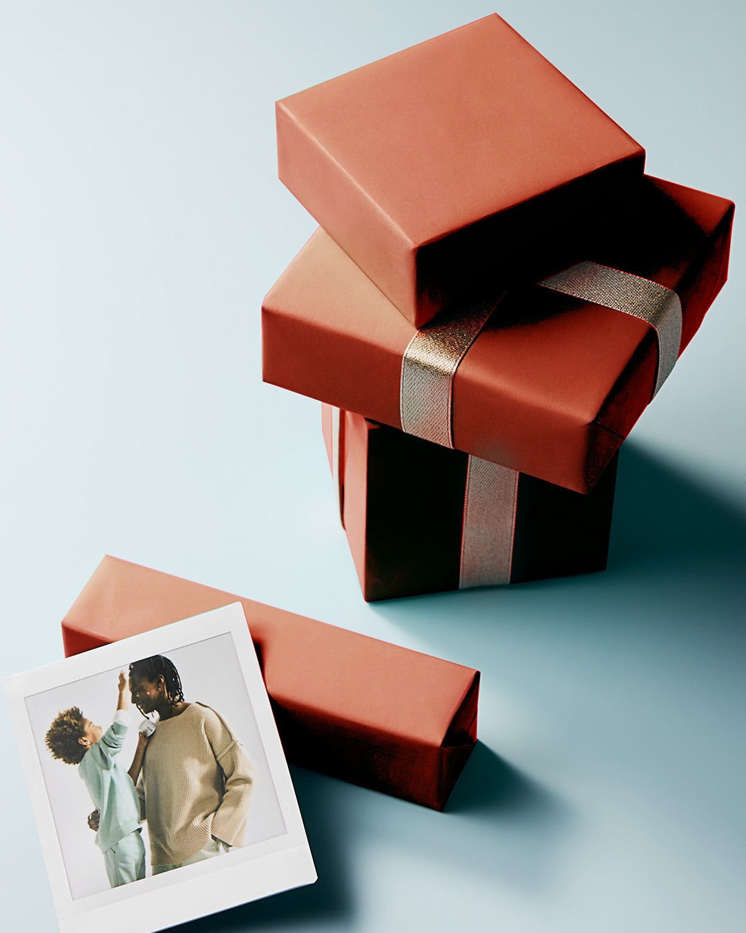 Découvrez une pile de cadeaux emballés dans du papier rouge-brun, ornés de rubans dorés et argentés, à côté d'une photo de famille.