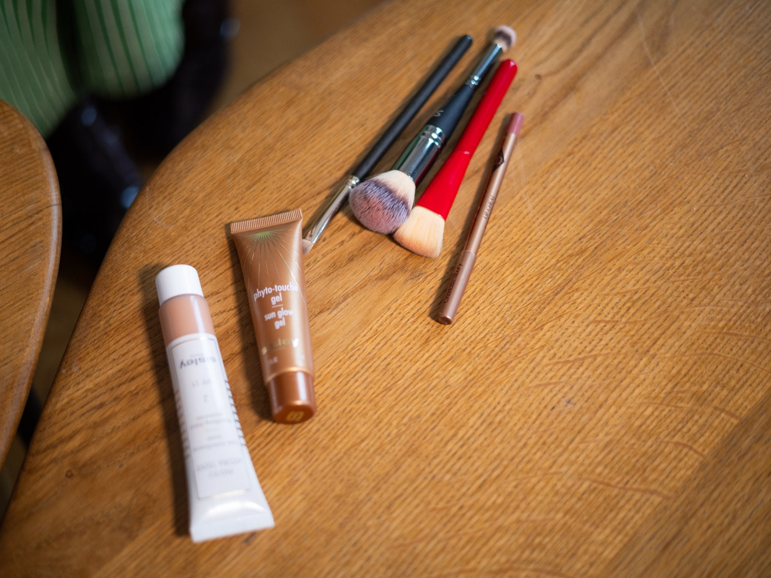 Sur une table en bois, découvrez un assortiment de produits de beauté : tubes de gel teinté, crayons à lèvres et pinceaux de maquillage.