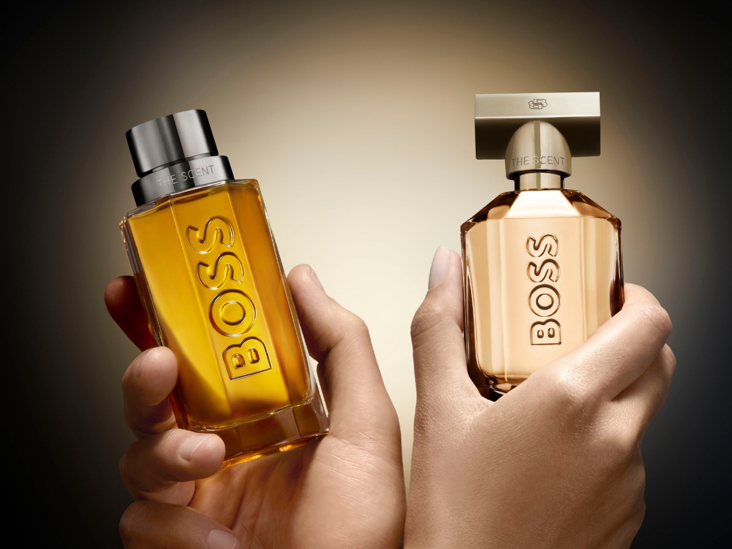 Dwa flakony perfum Boss: męski z bursztynowym płynem i srebrną nakrętką oraz damski w złotym flakonie z beżowym płynem i złotą nakrętką.