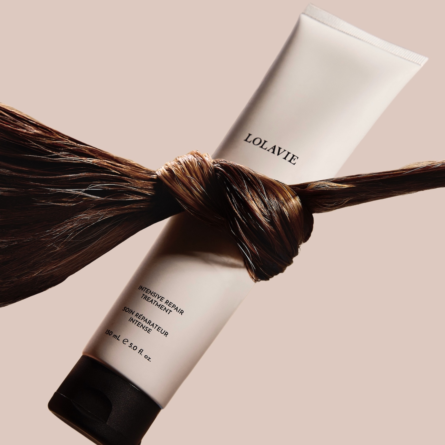 Tube blanc de soin réparateur intense LolaVie, noué par une mèche de cheveux bruns brillants, promettant une réparation en profondeur pour des cheveux éclatants de santé.