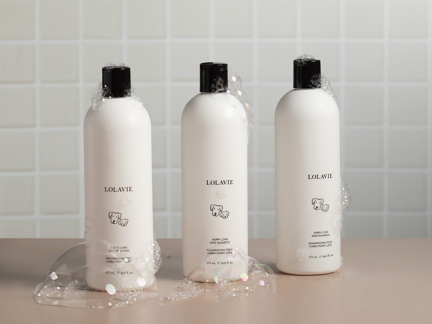Voici trois bouteilles blanches de shampoing pour chiens Lolavie, chacune ornée d'un bouchon noir et entourée de bulles, promettant un bain doux et agréable pour votre chiot.