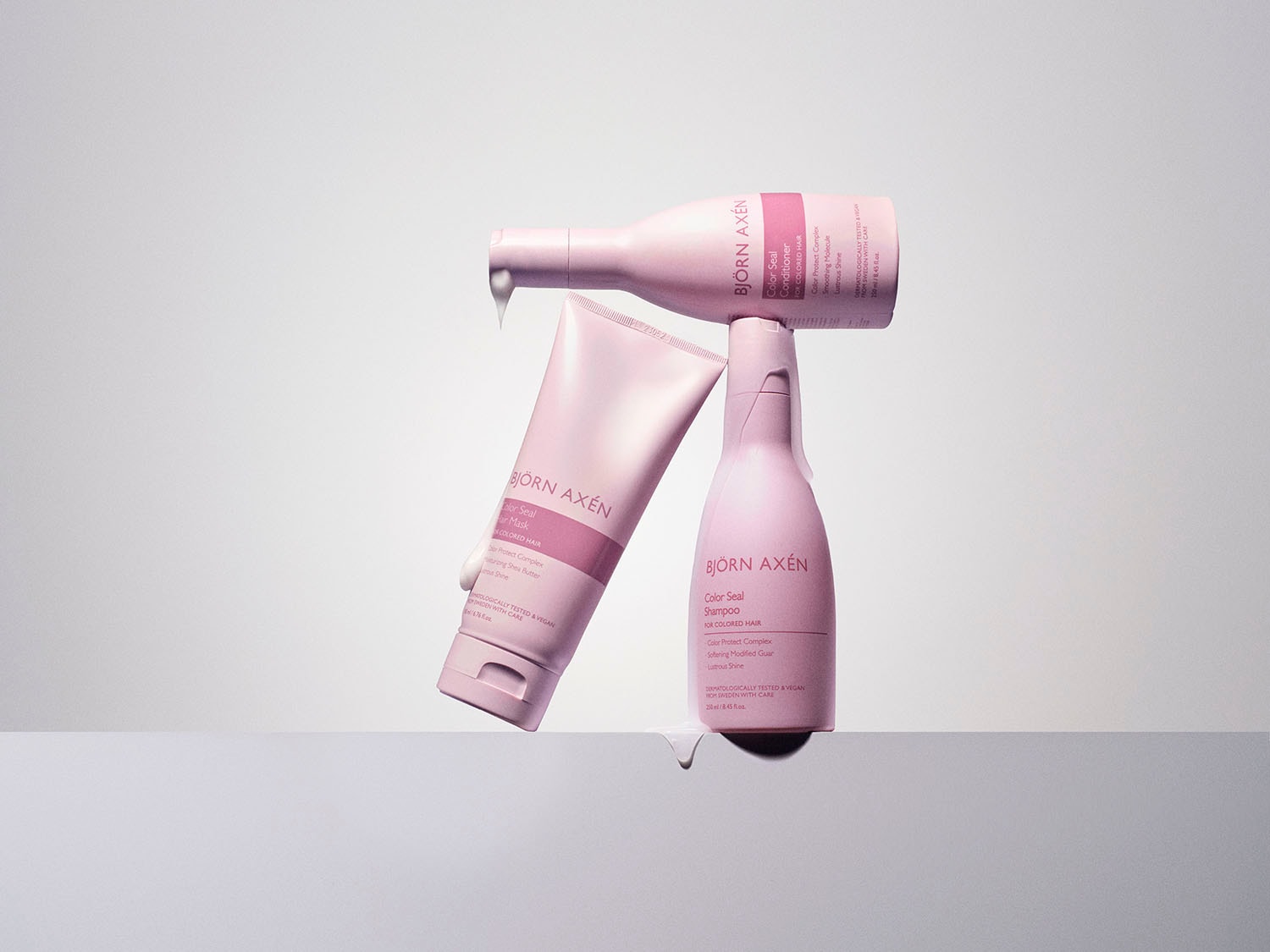 Różowe opakowania szamponu, odżywki i maski Björn Axén Color Seal do włosów farbowanych, obiecujące ochronę koloru, miękkość i blask.