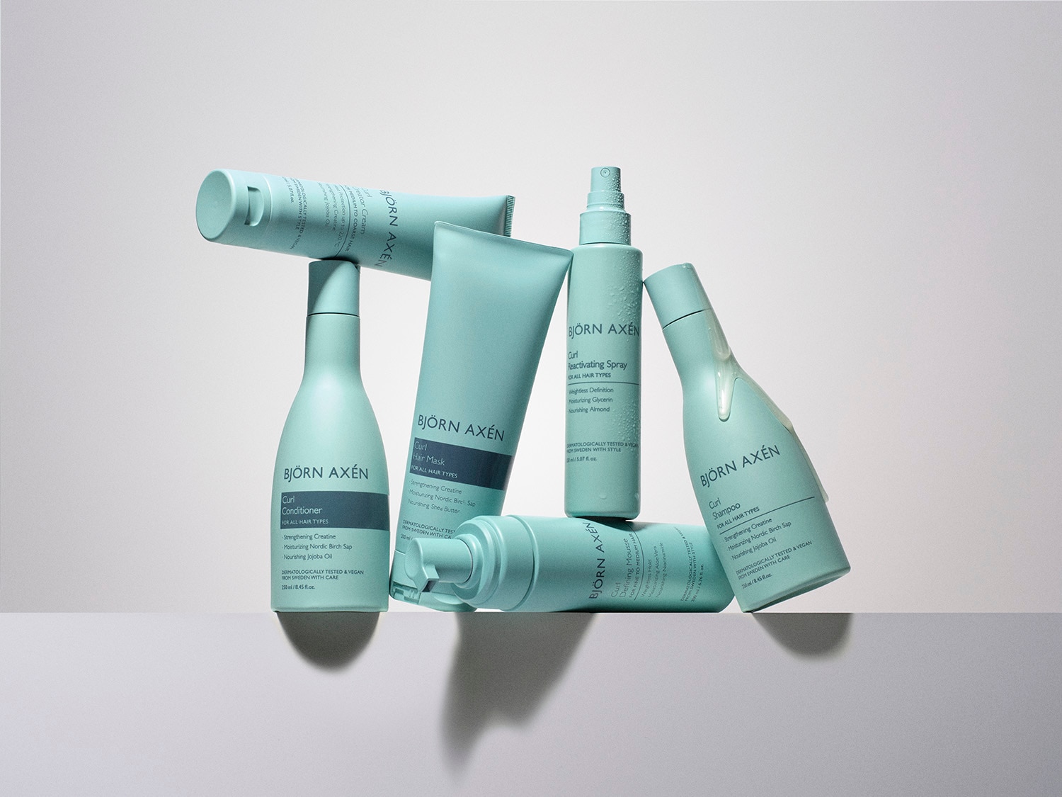 Zestaw produktów do włosów kręconych Björn Axén w turkusowych opakowaniach, zawierający szampon, odżywkę, maskę, spray reaktywujący i piankę definiującą.