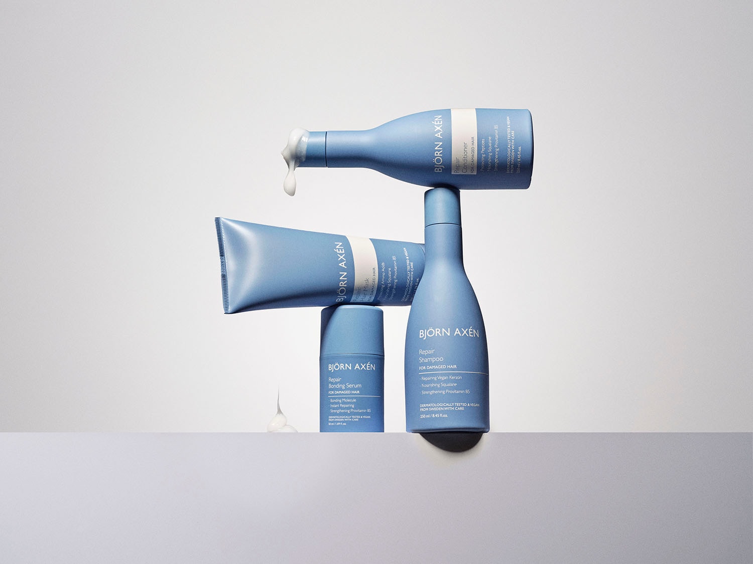 Na zdjęciu widać zestaw produktów do pielęgnacji włosów Björn Axén Repair w jasnoniebieskich opakowaniach: szampon, odżywkę, maskę i serum, przeznaczonych do włosów zniszczonych.