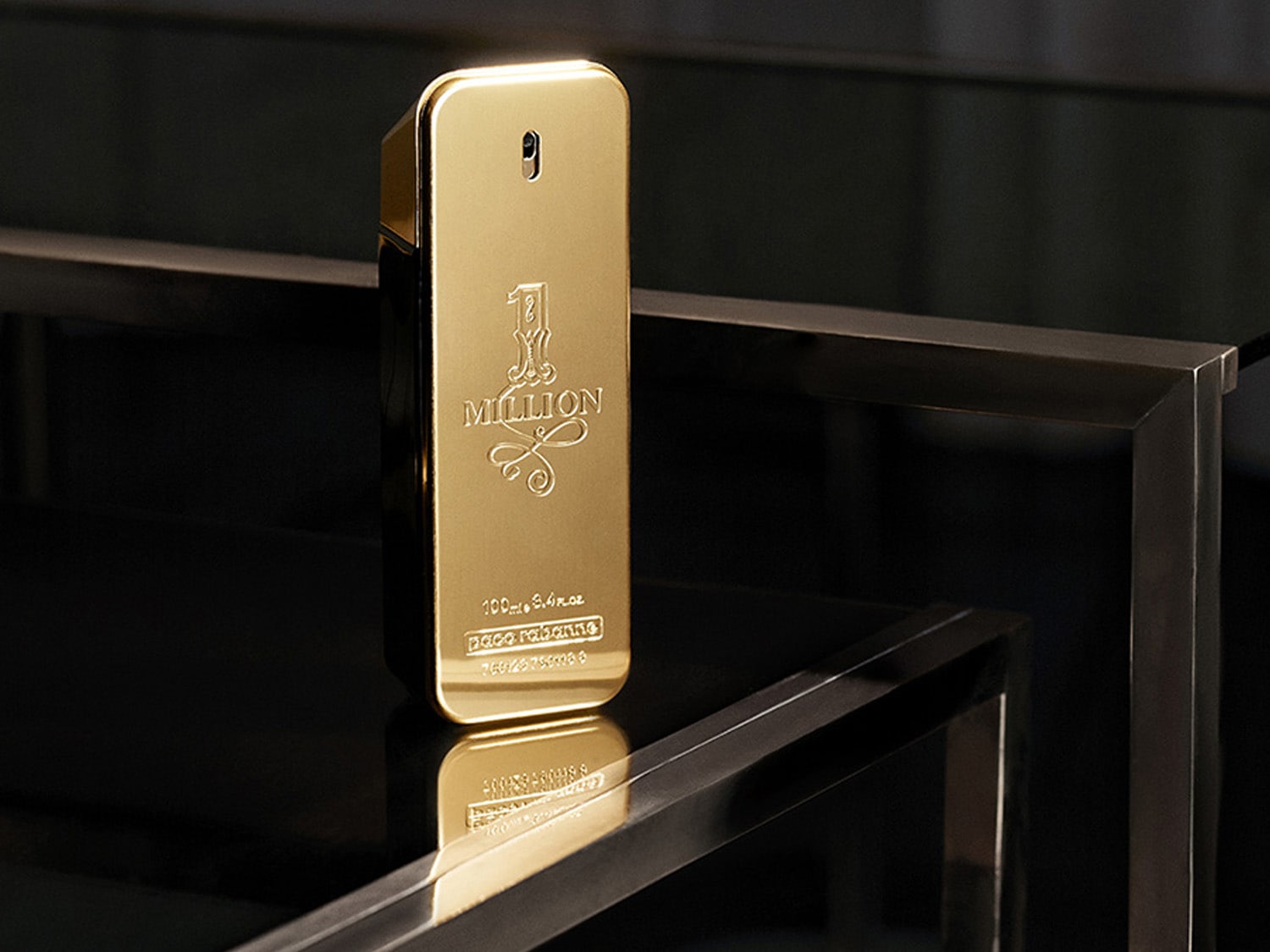 Zlatý flakon parfému 1 Million od Paco Rabanne stojí na lesklém černém povrchu a odráží se v něm.