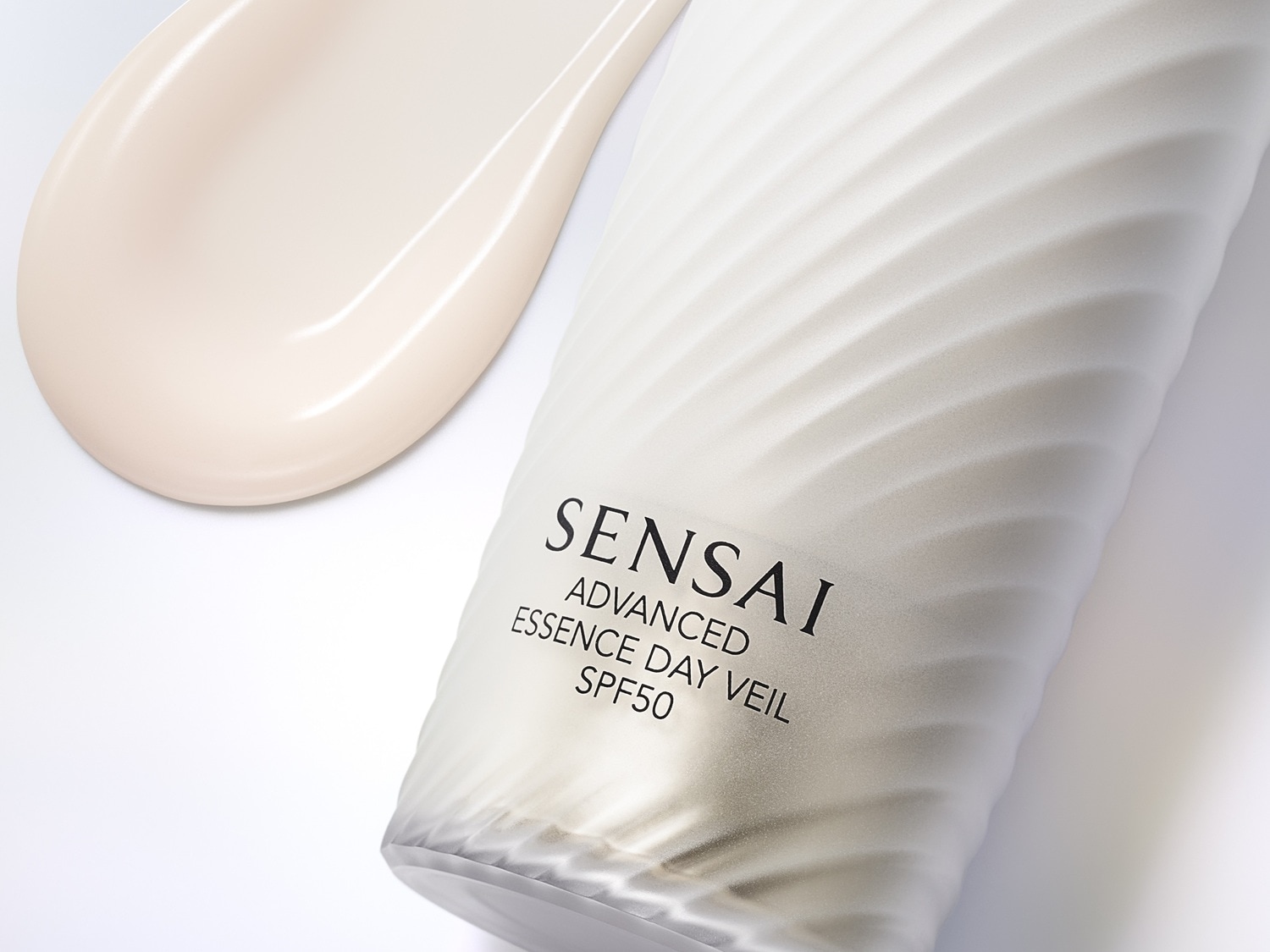Krem Sensai Advanced Essence Day Veil SPF50 w białym opakowaniu z beżową kroplą kremu obok, zapewniający zaawansowaną ochronę i pielęgnację skóry.