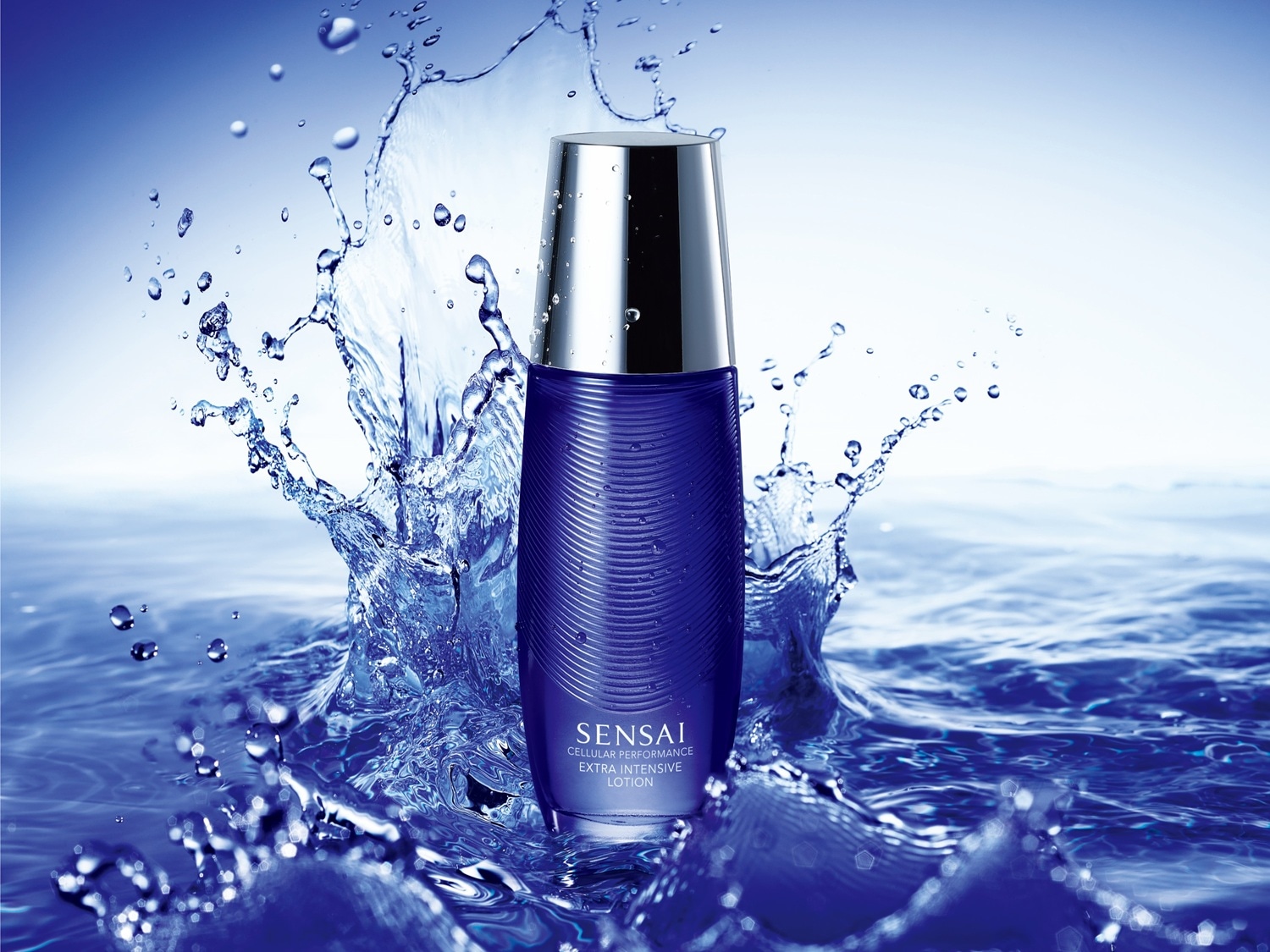 Butelka Sensai Cellular Performance Extra Intensive Lotion w niebieskim opakowaniu z srebrną nakrętką, otoczona rozpryskującą się wodą, co sugeruje intensywne nawilżenie i odświeżenie skóry.