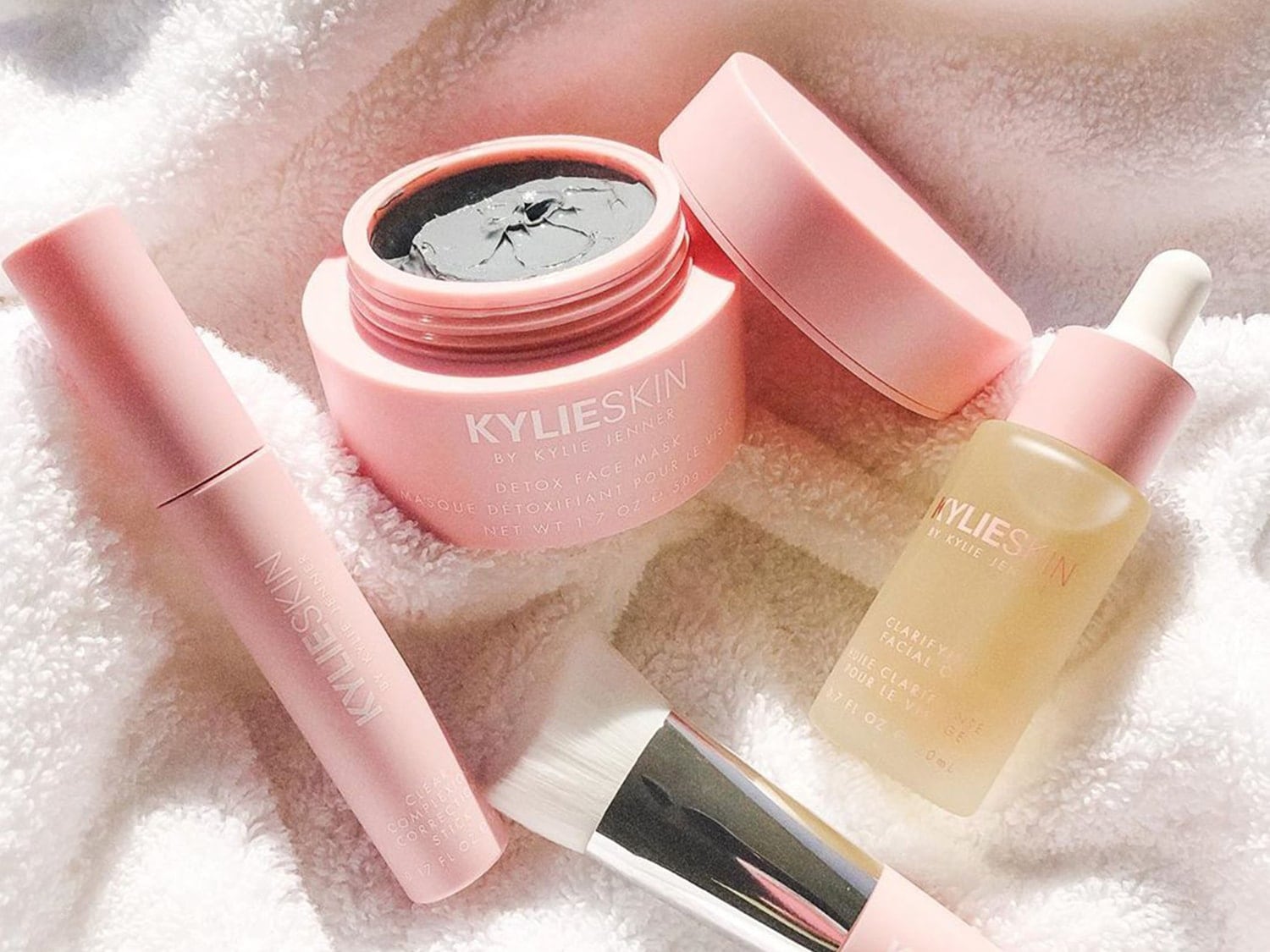 Découvrez les produits de soin de la peau KylieSkin, comprenant un masque détoxifiant, un stick correcteur de teint et une huile clarifiante pour le visage, présentés dans des emballages roses doux.