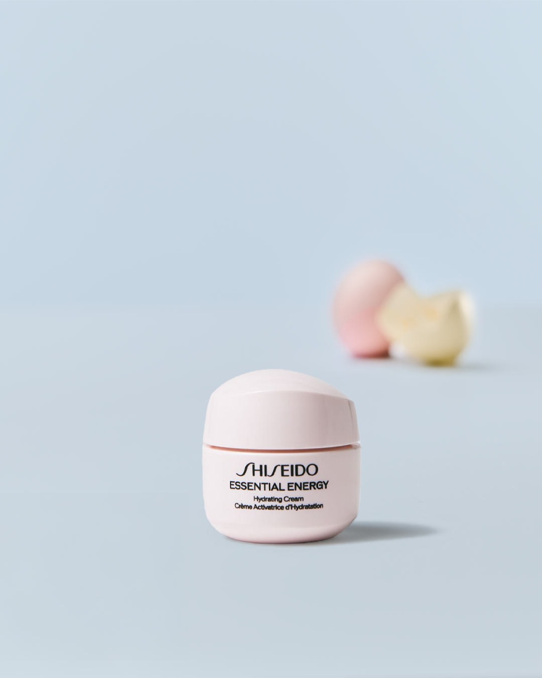 Nahaufnahme einer kleinen, runden, hellrosa Dose Shiseido Essential Energy Hydrating Cream, die auf einer hellblauen Oberfläche steht.