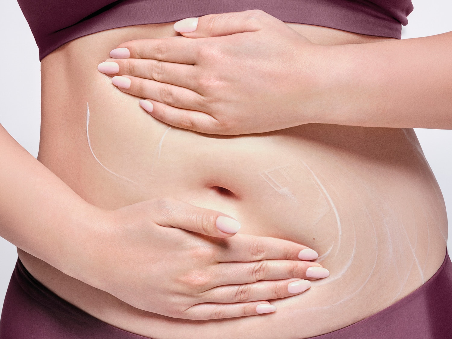 Mani che massaggiano delicatamente la crema bianca sulla pancia, creando un'esperienza sensoriale avvolgente.