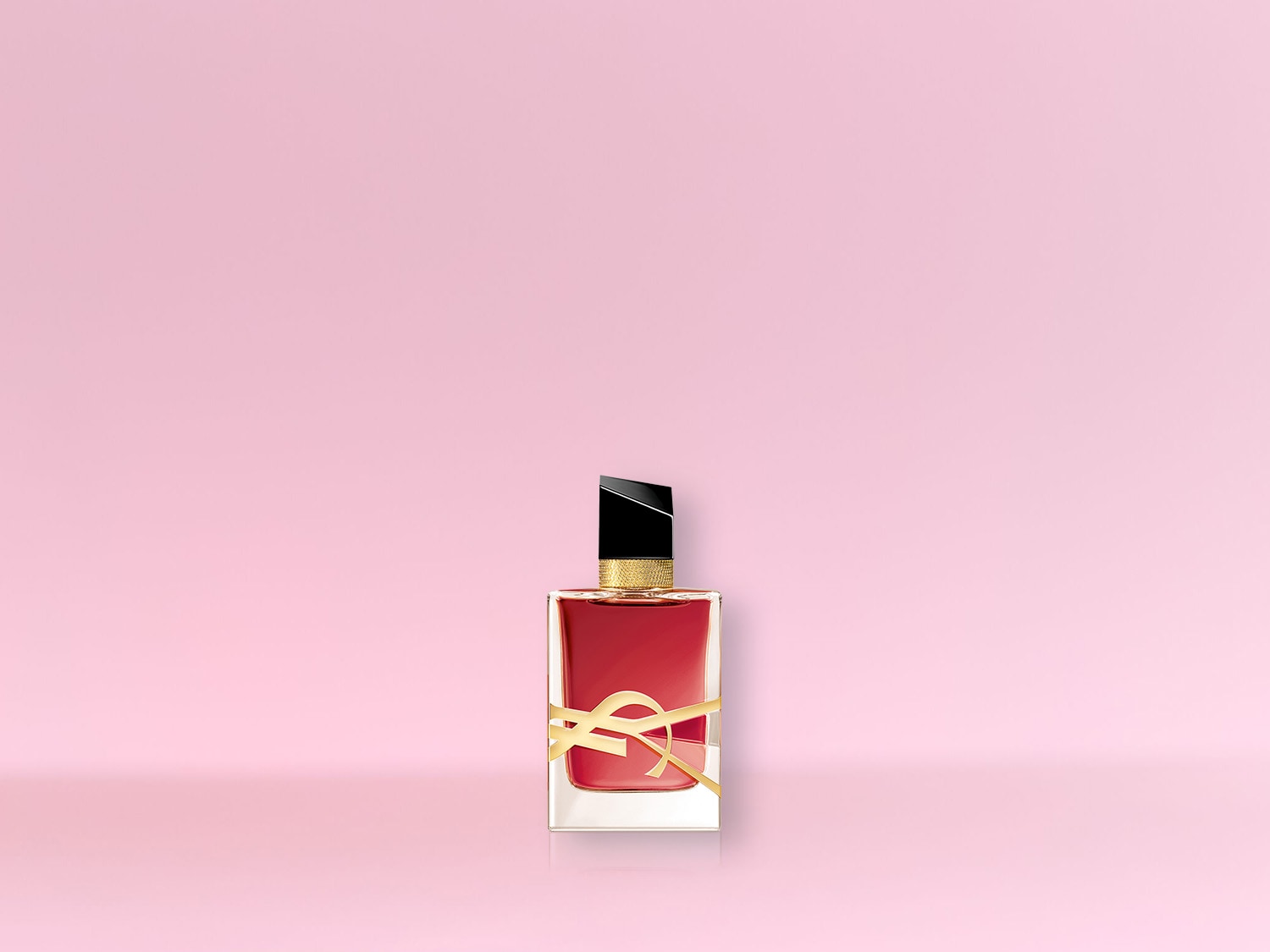 Ein rechteckiger, transparenter Flakon mit rotem Inhalt und goldenem YSL-Logo steht vor einem zarten rosa Hintergrund.