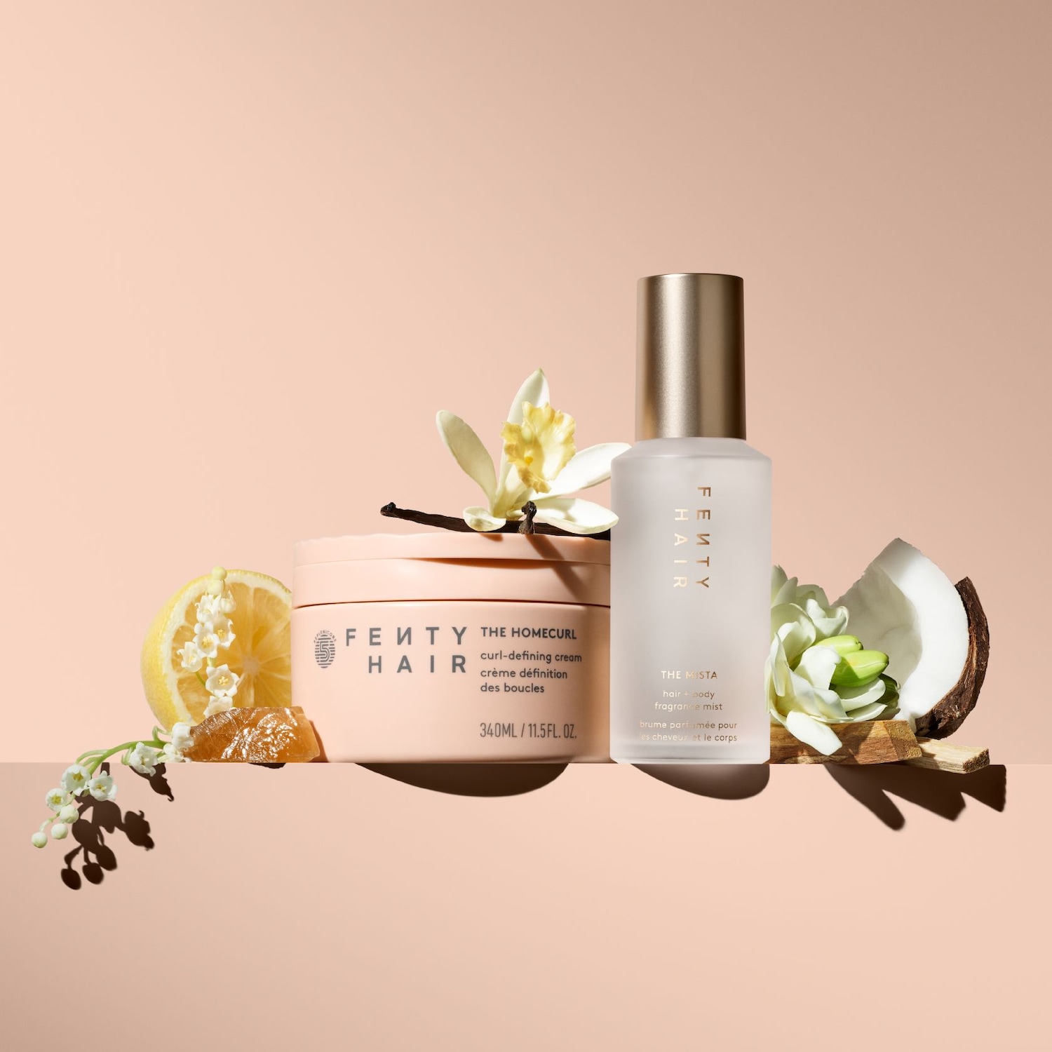 FENTY Hair The Homecurl curl-defining cream in een roze verpakking, samen met The Mista hair & body fragrance mist, gepresenteerd met citroen, kokosnoot en vanillebloemen.