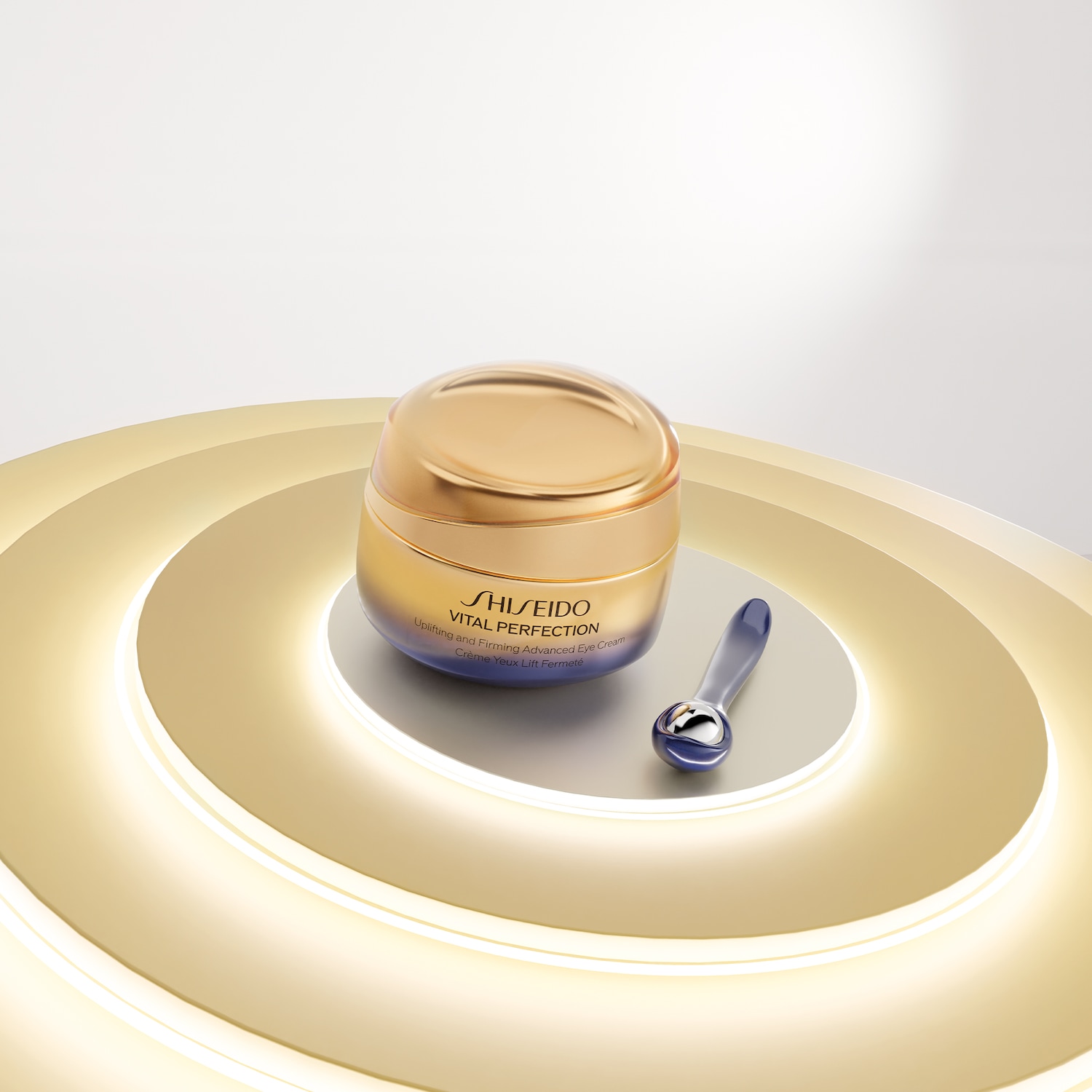 Un barattolo dorato di crema per gli occhi Shiseido Vital Perfection, con un applicatore blu, su una piattaforma dorata illuminata.