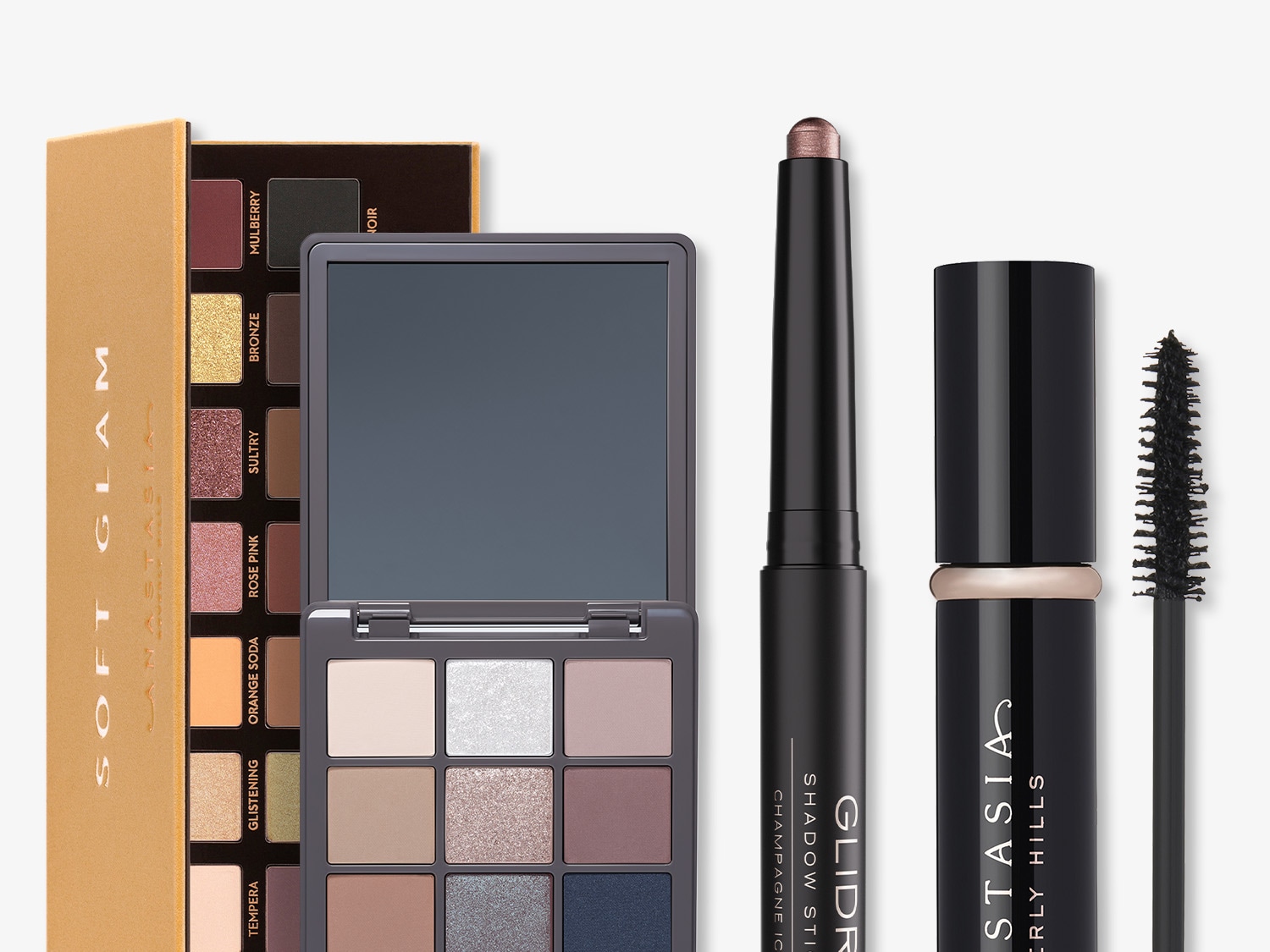 The image showcases Anastasia Beverly Hills makeup products, including Soft Glam eyeshadow palette with shades like Mulberry and Bronze, Glidr Shadow Stick in Champagne Ice, and a black mascara for a complete eye look.
