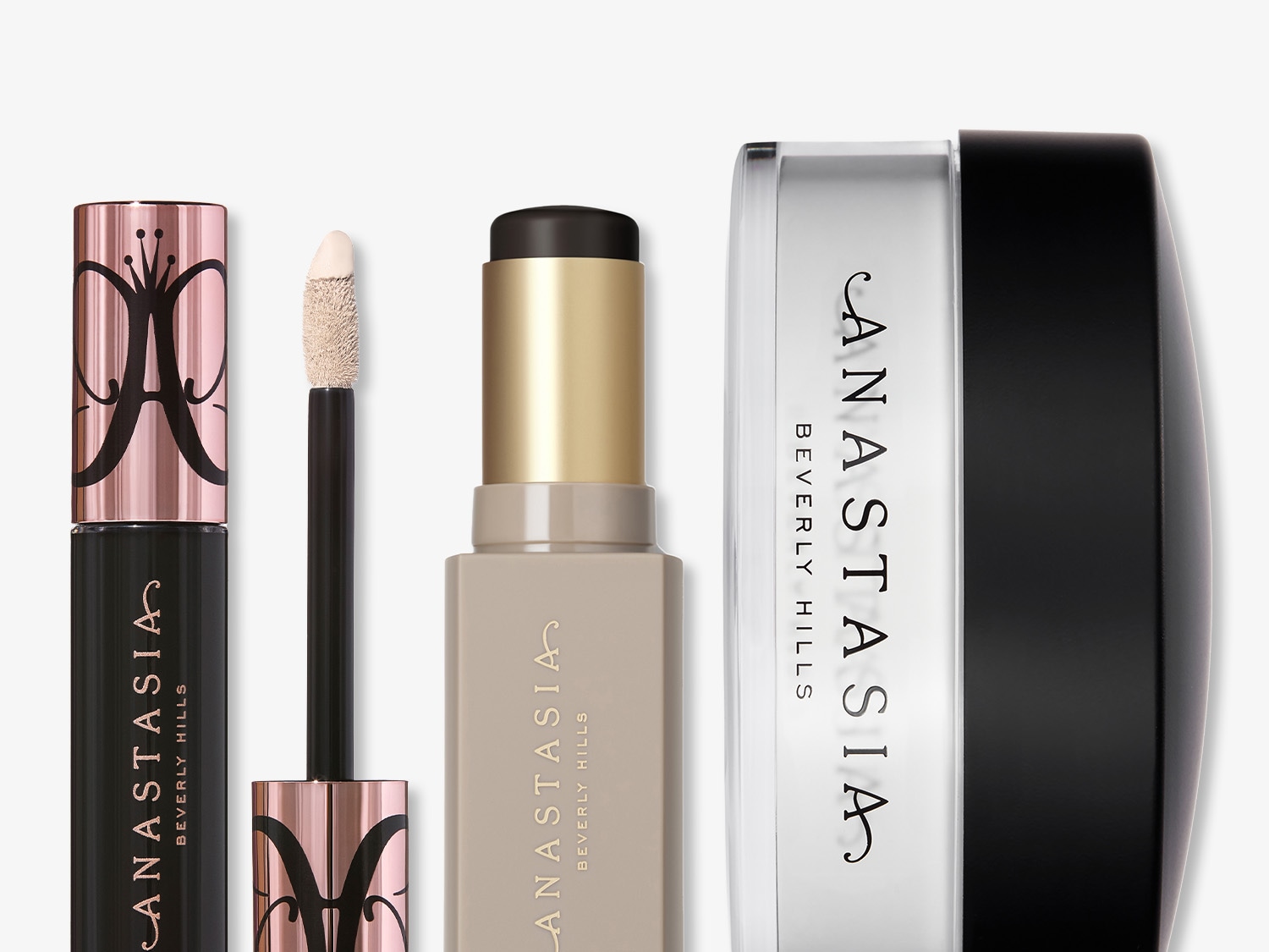 Anastasia Beverly Hills makeup set includes a black tube with a rose gold cap, a concealer with a wand, a beige stick with a gold cap, and a translucent powder with a black lid.