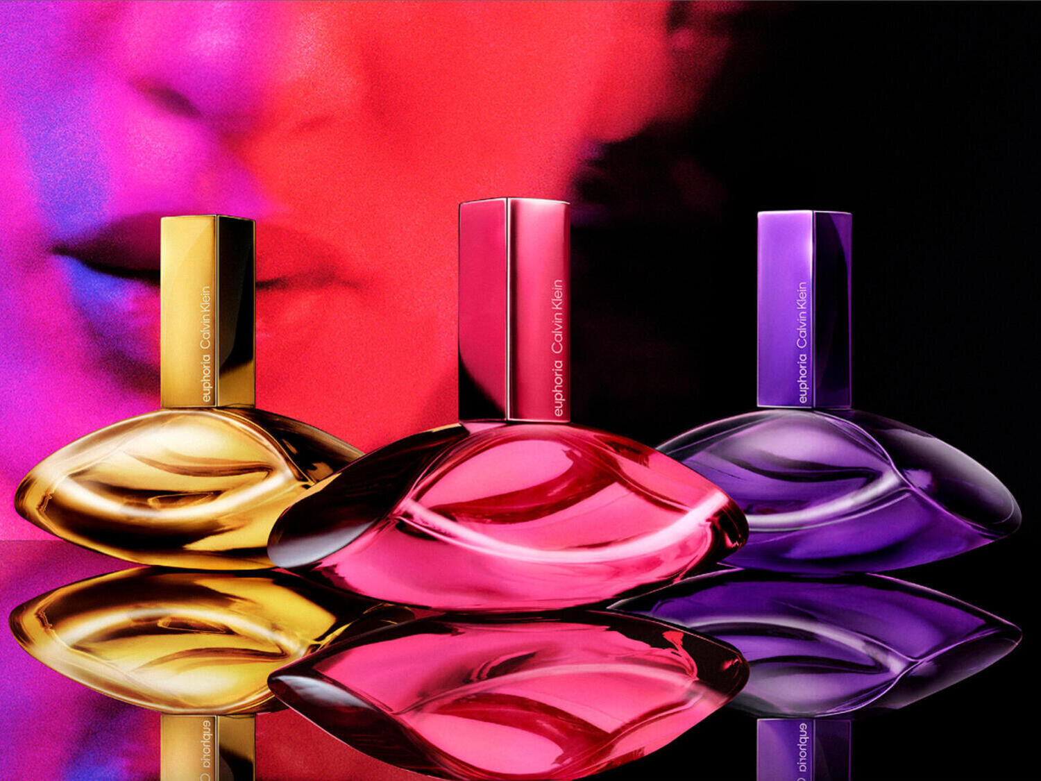 Tres frascos de perfume Euphoria de Calvin Klein en dorado, rosa y morado, reflejados sobre una superficie brillante, con un fondo abstracto en tonos rojos y púrpuras.