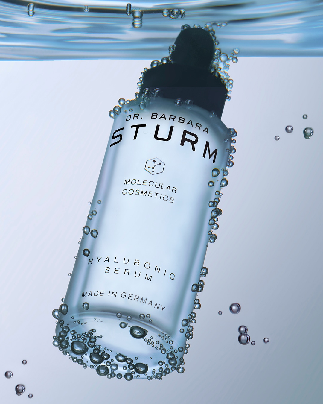 Das Hyaluronic Serum von Dr. Barbara Sturm in einer durchsichtigen Flasche mit Pipette, umgeben von Wassertropfen, verspricht viel Feuchtigkeit für die Haut.