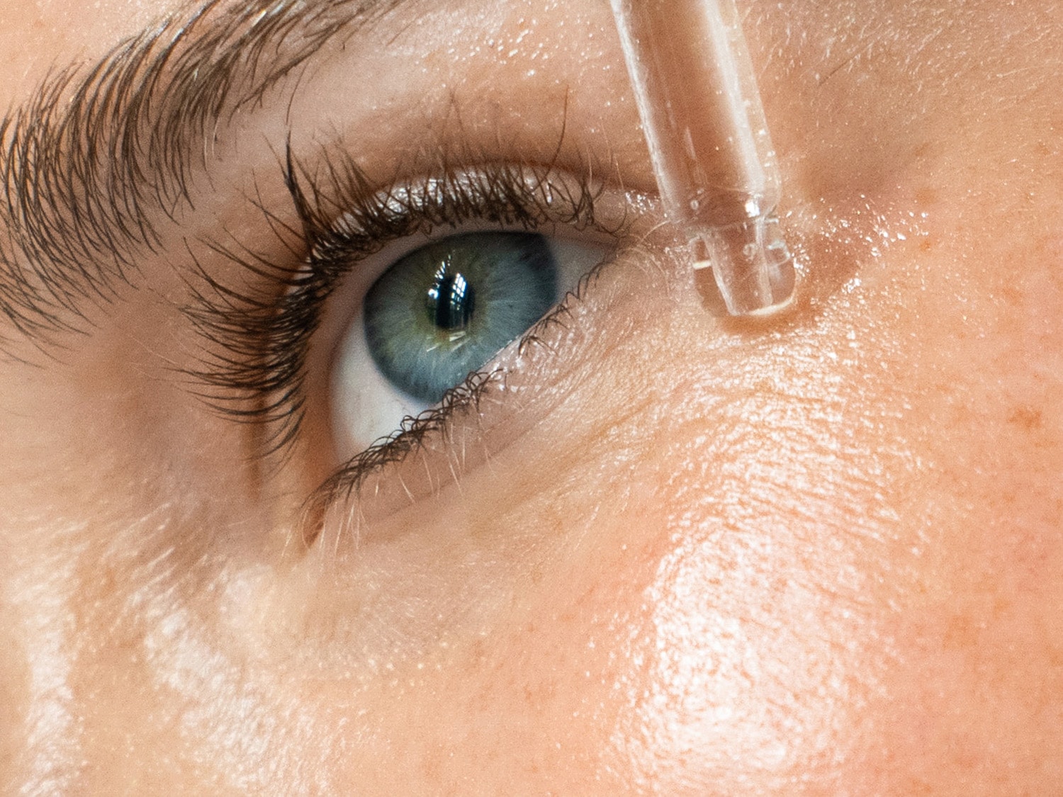 Nahaufnahme eines Auges mit einer Pipette, die ein klares Serum auf die Haut aufträgt, um die feuchtigkeitsspendende Wirkung hervorzuheben.