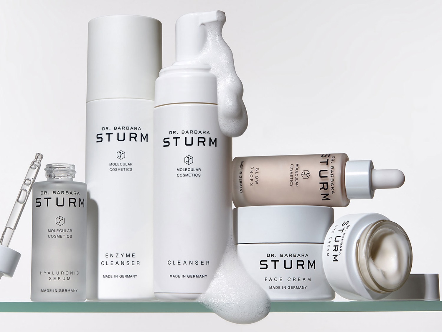 Eine Kollektion an Hautpflegeprodukten von Dr. Barbara Sturm, darunter Hyaluronsäure-Serum, Enzymreiniger, Gesichtsreiniger, Glow Drops, Gesichtscreme und Augencreme, alle in minimalistischen weißen Verpackungen.