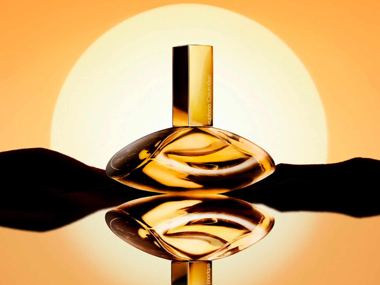 Bursztynowy flakon perfum Calvin Klein Euphoria odbija się w wodzie na tle zachodzącego słońca, tworząc ciepłą i zmysłową aurę.