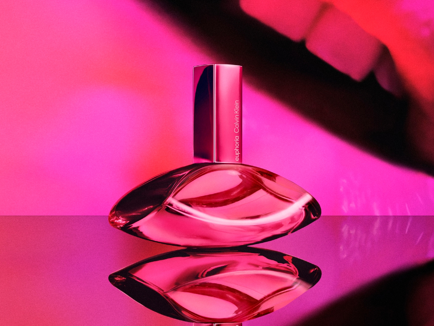 Różowy flakon perfum Calvin Klein Euphoria o pojemności 100 ml, z metaliczną nakrętką, odbija się na błyszczącej powierzchni na tle w odcieniach różu.