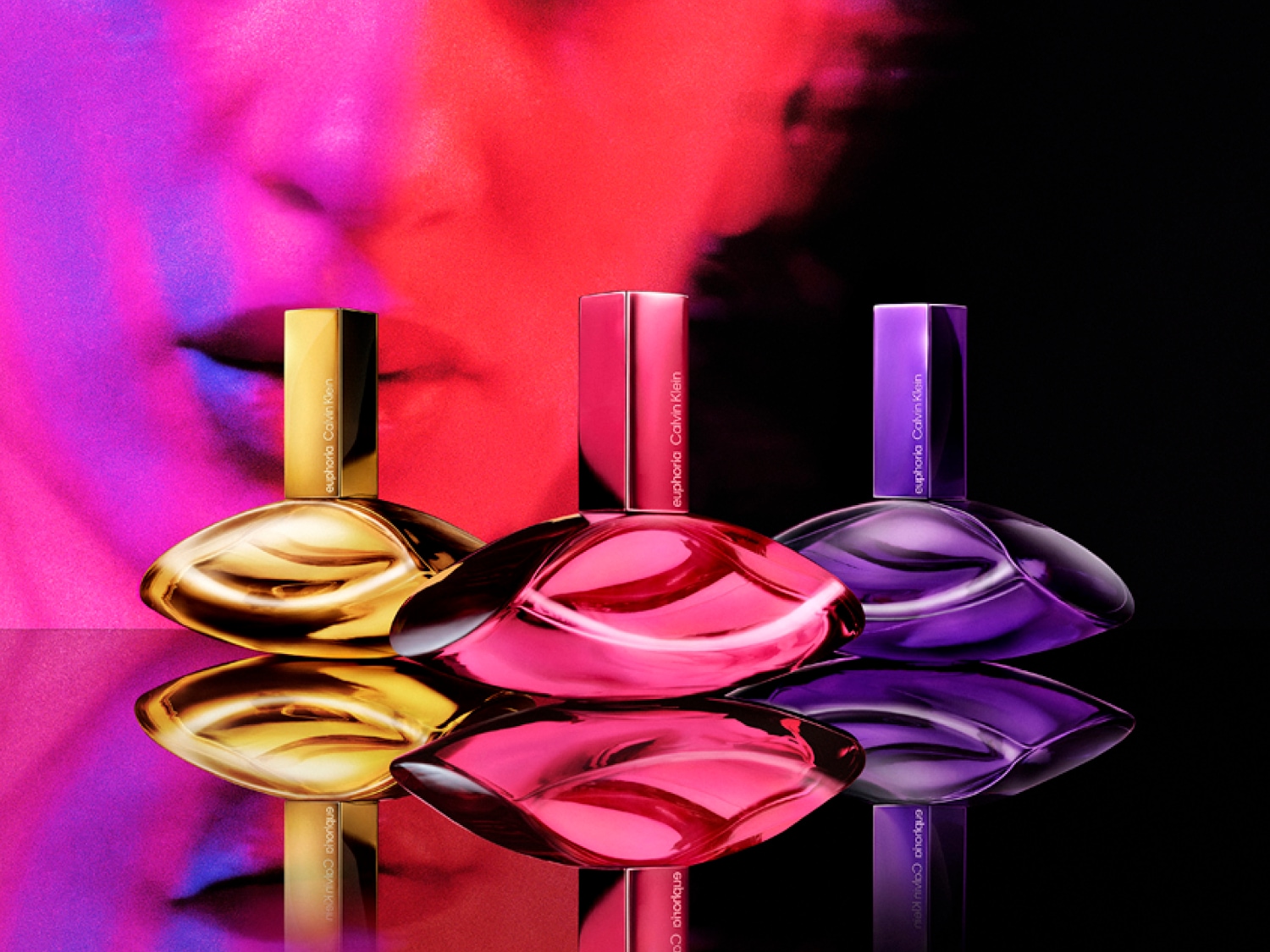 Trzy flakony perfum Calvin Klein Euphoria w kolorach złotym, różowym i fioletowym, odbijające się w błyszczącej powierzchni, na tle twarzy w odcieniach różu i fioletu.