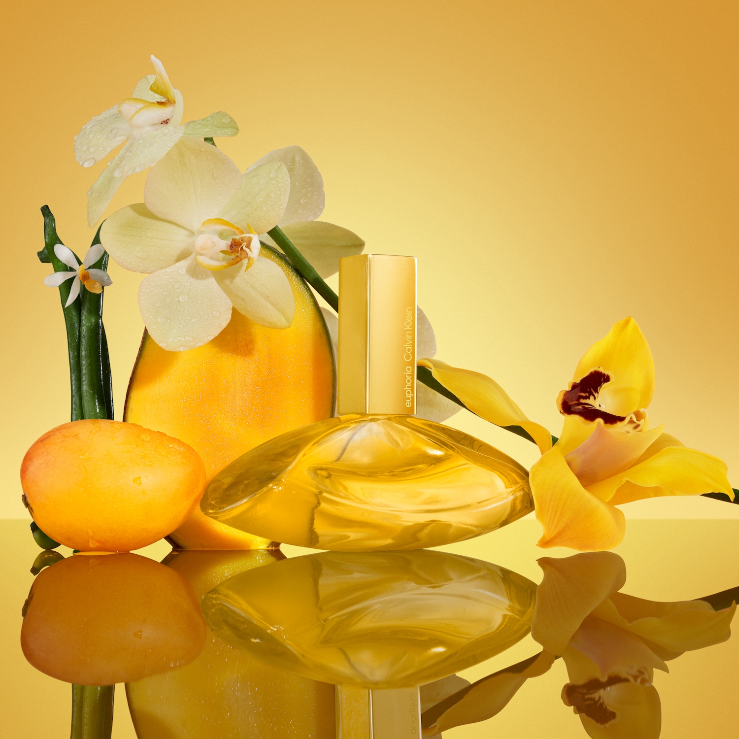 Żółty flakon perfum Euphoria Calvin Klein otoczony mango i kwiatami orchidei na złotym tle, tworzący ciepłą i egzotyczną kompozycję.