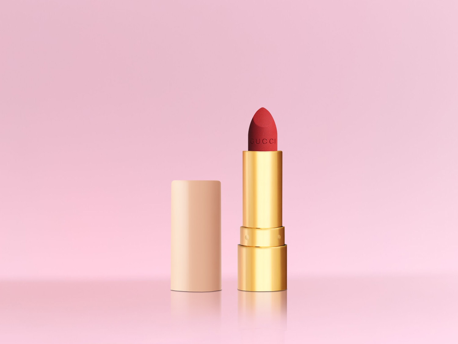 Ein roter Gucci Lippenstift mit goldener Hülle und beiger Kappe steht vor einem rosa Hintergrund.