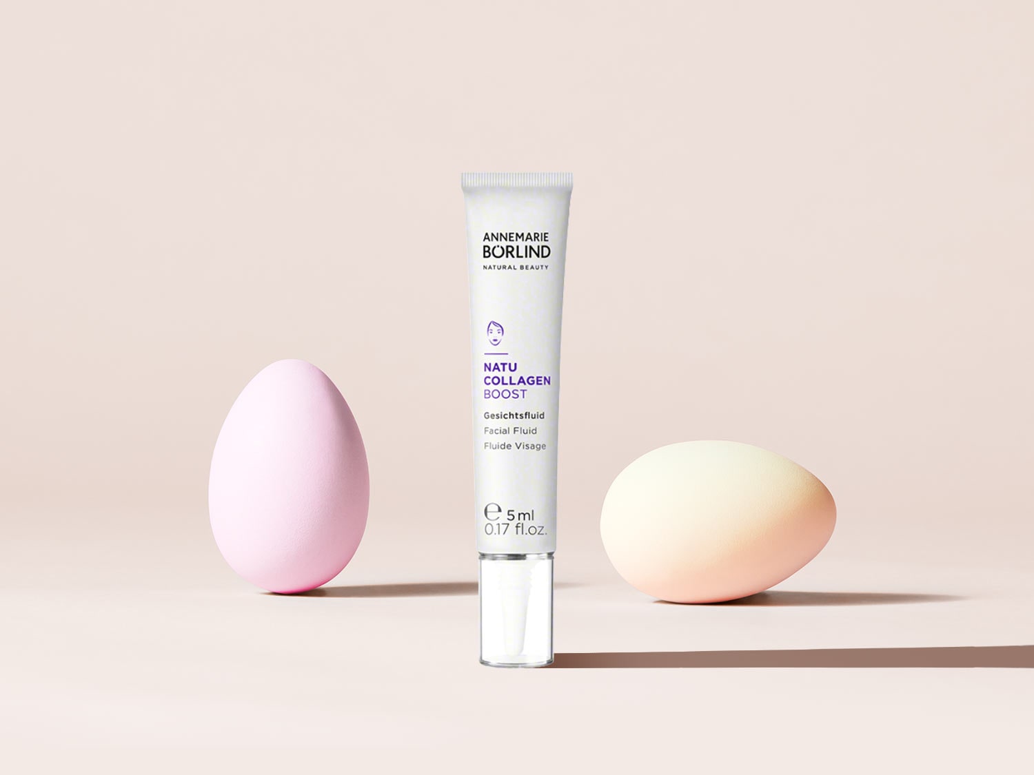 Das Annemarie Börlind Natu Collagen Boost Gesichtsfluid in einer weißen Tube mit 5 ml Inhalt, umgeben von zwei pastellfarbenen Eiern.