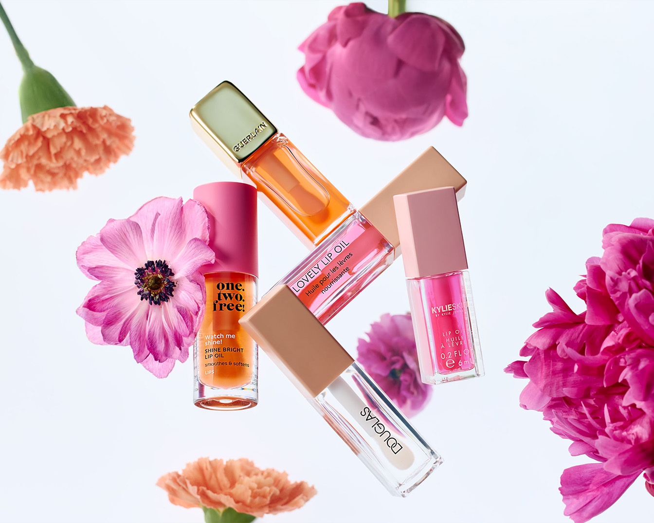 Verschiedene Lippenöle von Marken wie Guerlain, Douglas und Kylie Skin sind mit bunten Blüten auf einem weißen Hintergrund arrangiert.