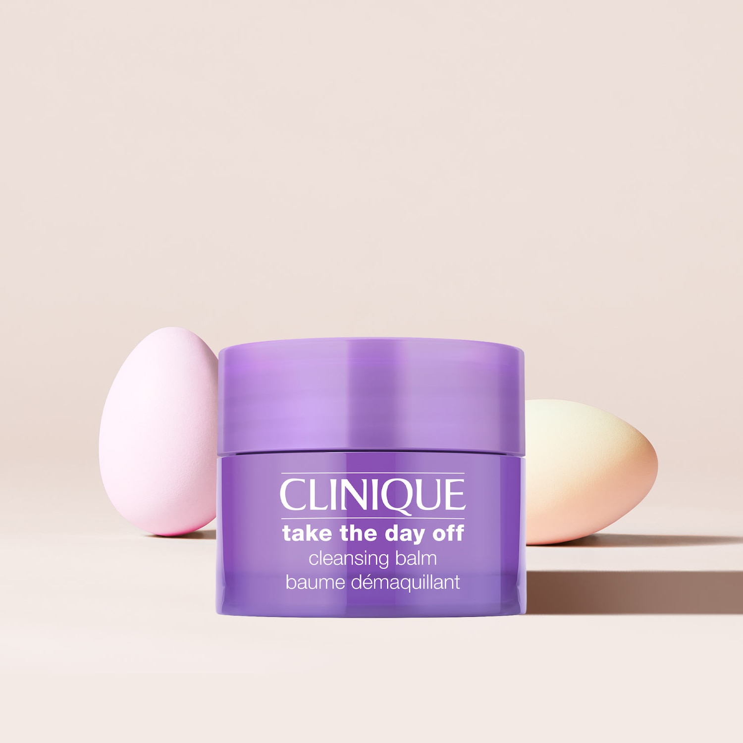 Nahaufnahme eines lila Clinique "Take the day off" Reinigungsbalsams in einer Dose mit zwei Make-up-Eiern im Hintergrund.