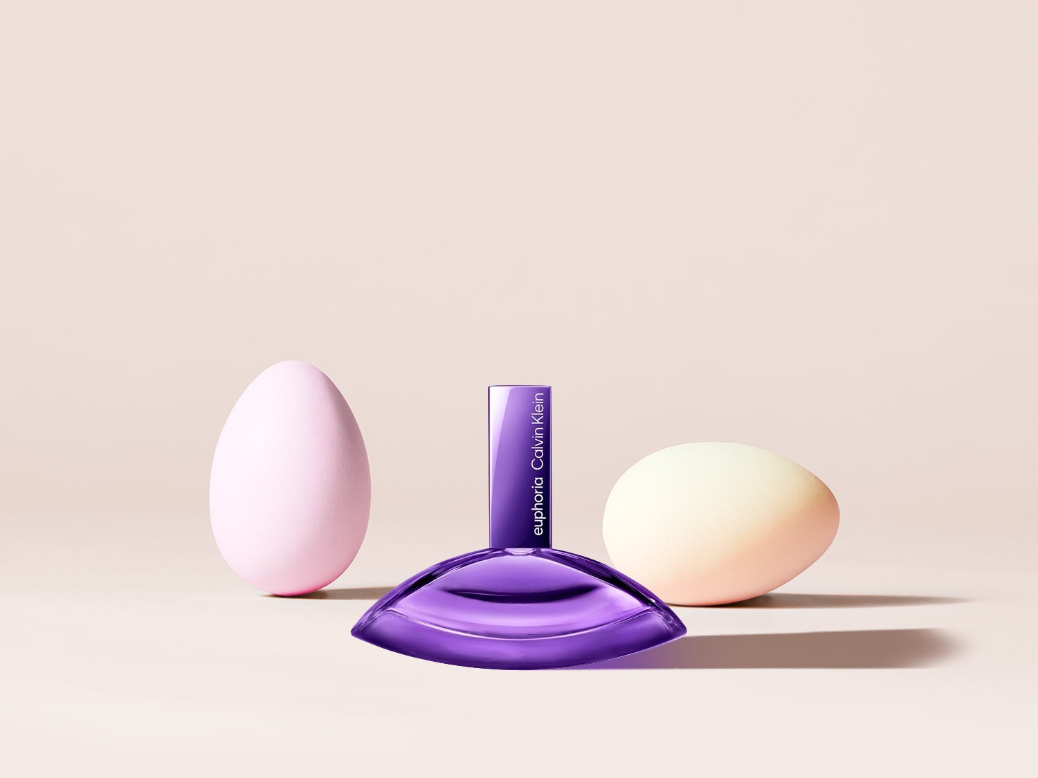 Ein violetter Calvin Klein Euphoria-Duft steht zwischen zwei pastellfarbenen Ostereiern und versprüht einen Hauch von Frühling.