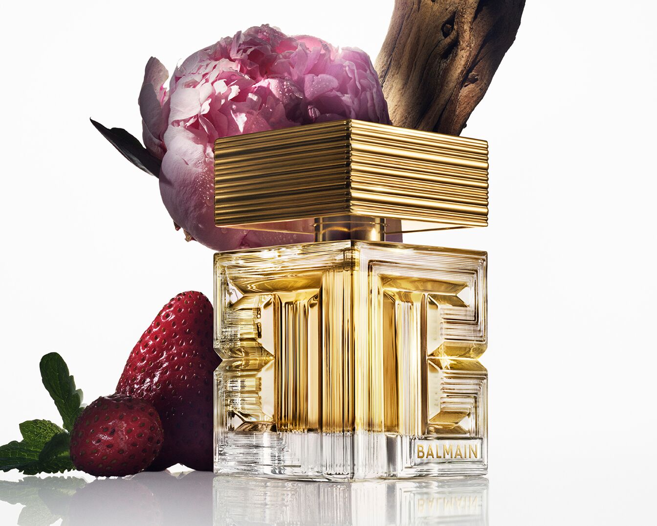 Découvrez le parfum Balmain dans son flacon doré distinctif, agrémenté d'une pivoine rose, de fraises et d'une touche de bois, une essence de luxe et de nature.