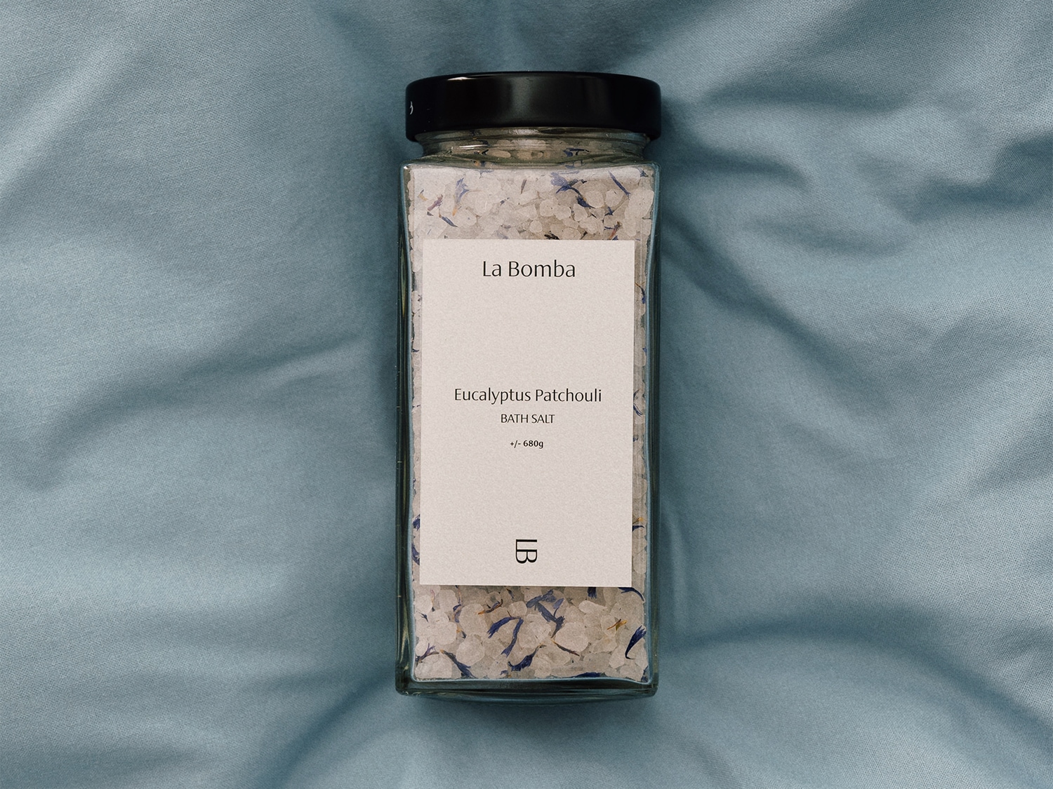 Słoik soli do kąpieli La Bomba o zapachu eukaliptusa i paczuli, zawierający białe kryształki soli i niebieskie płatki kwiatów.