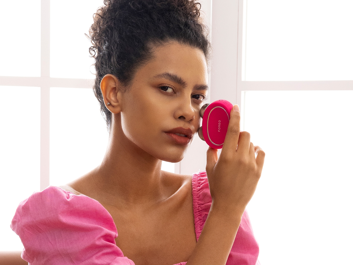 Une femme utilise un appareil de massage facial rose de marque FOREO, pour une peau éclatante et revitalisée.