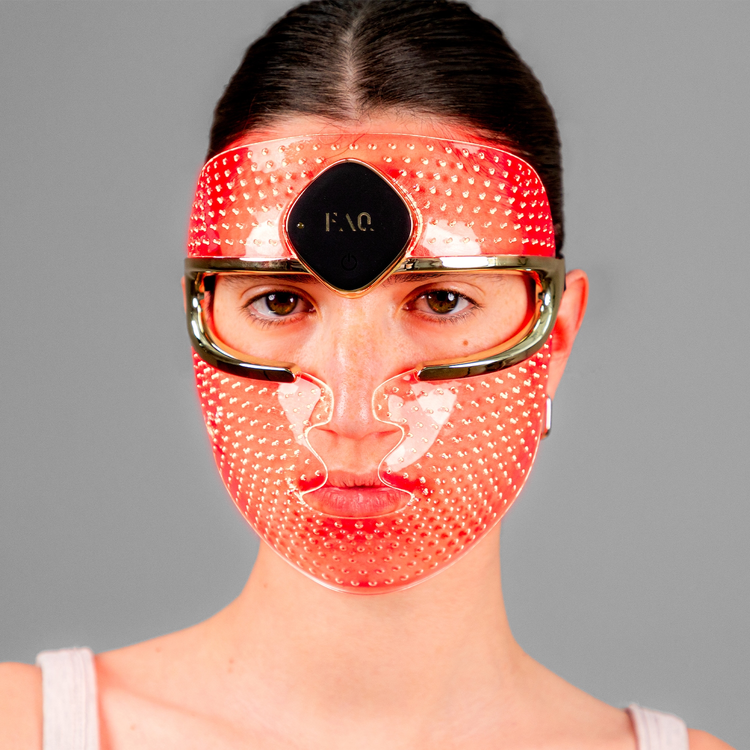 Portrait d'une femme portant un masque facial LED rouge transparent avec des accents dorés, conçu pour les soins de la peau.