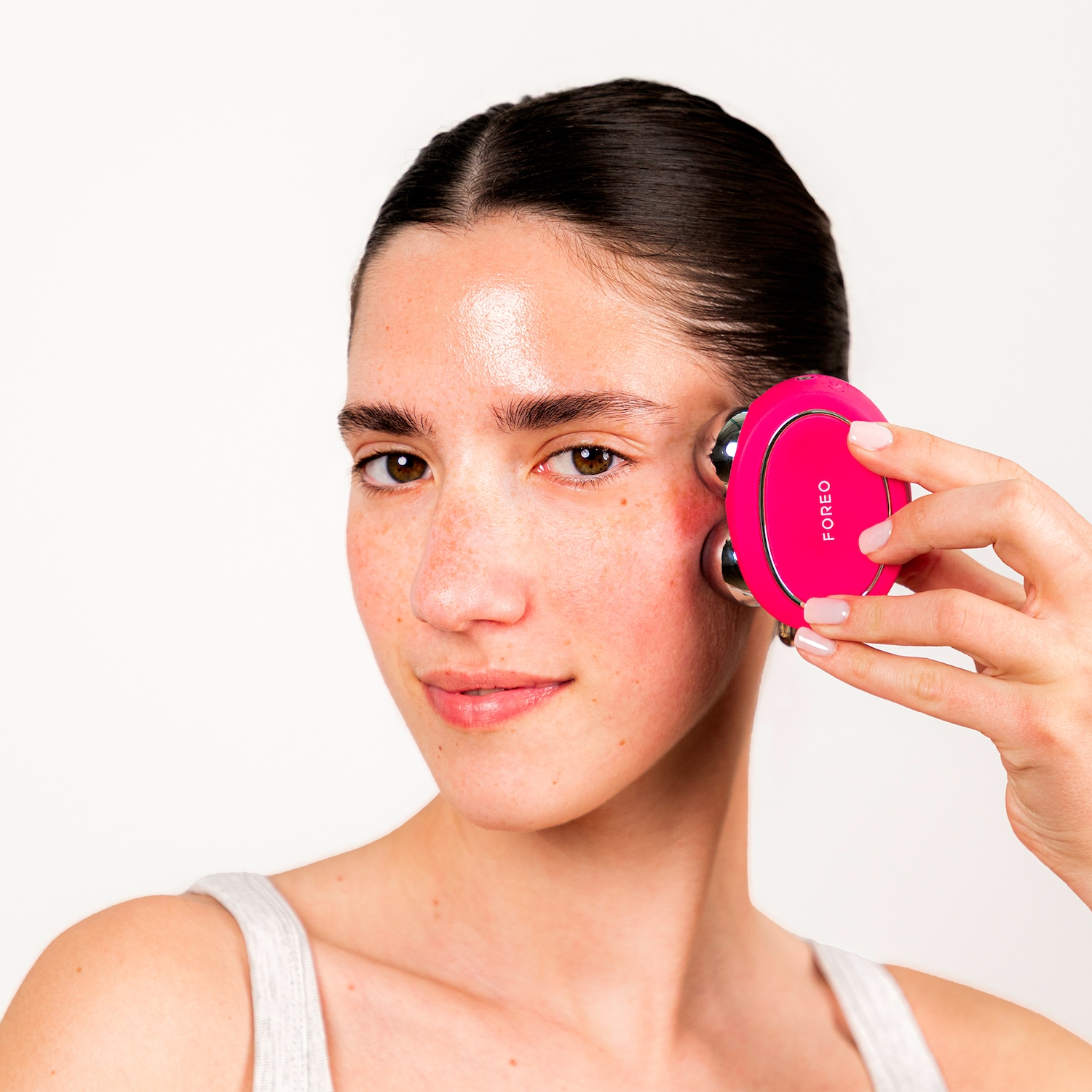 Une femme utilise un appareil de massage facial rose de la marque FOREO sur sa joue pour un soin de la peau.