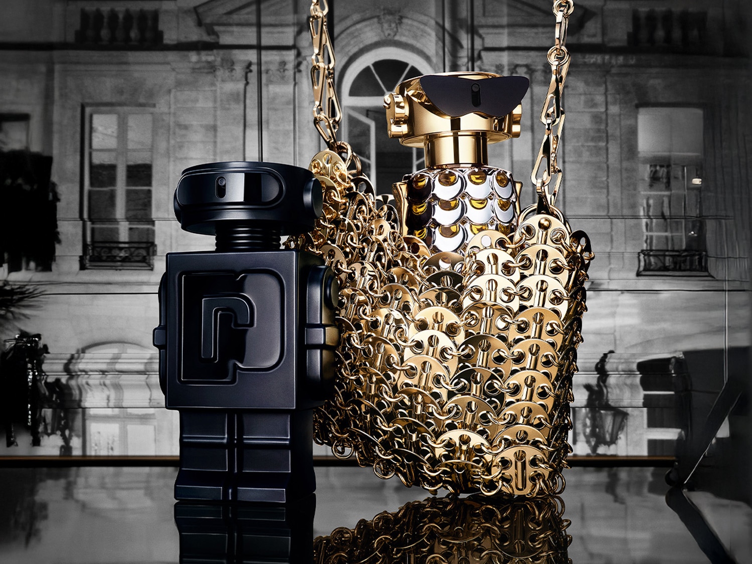 Dva flakóny vôní, jeden v tvare robota v čiernej farbe a druhý v zlatej retiazke, stoja vedľa seba na lesklom povrchu.